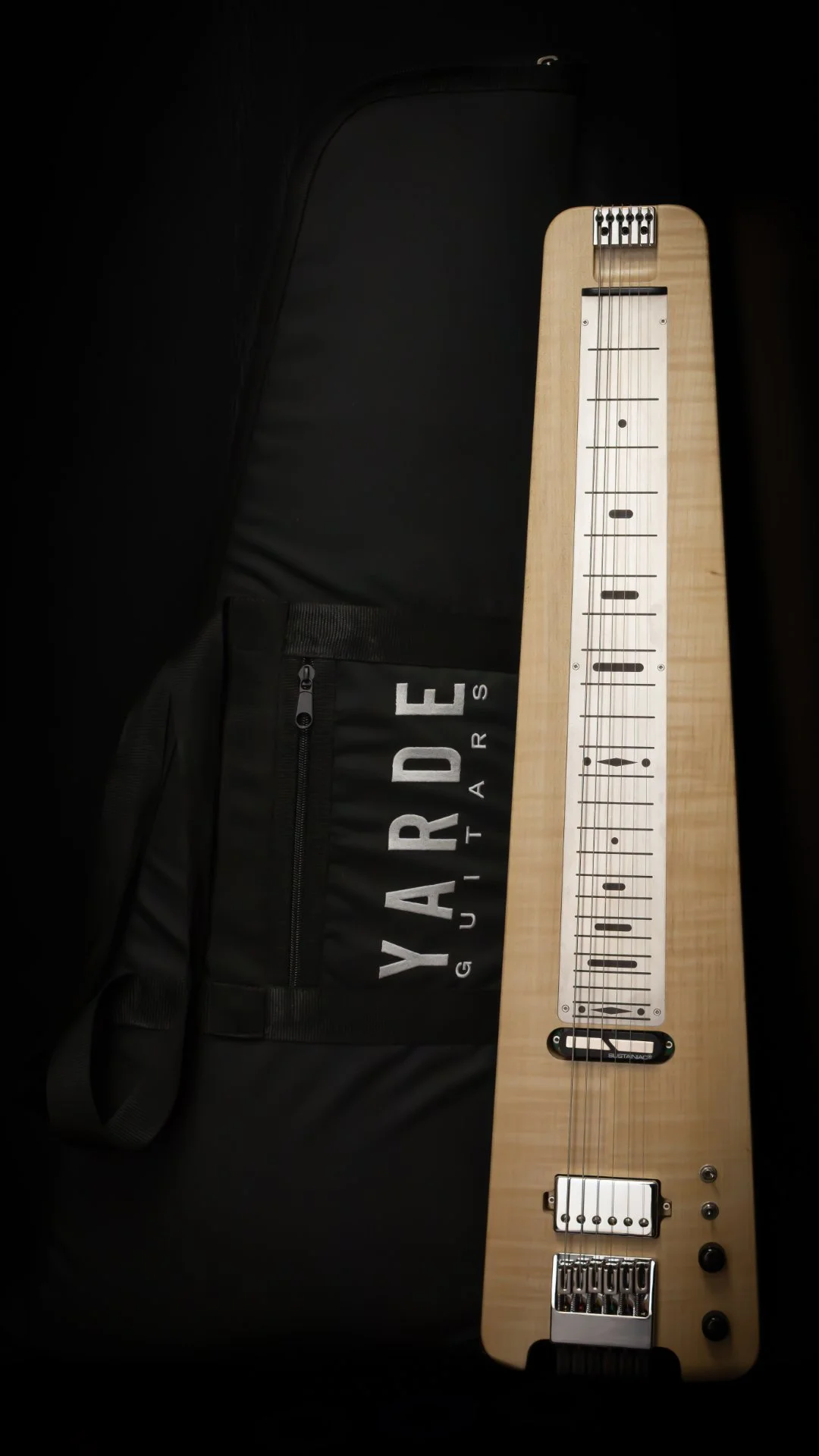 A modern headless lapsteel leaning on a 'Yarde Guitars' branded gig bag against a black background
