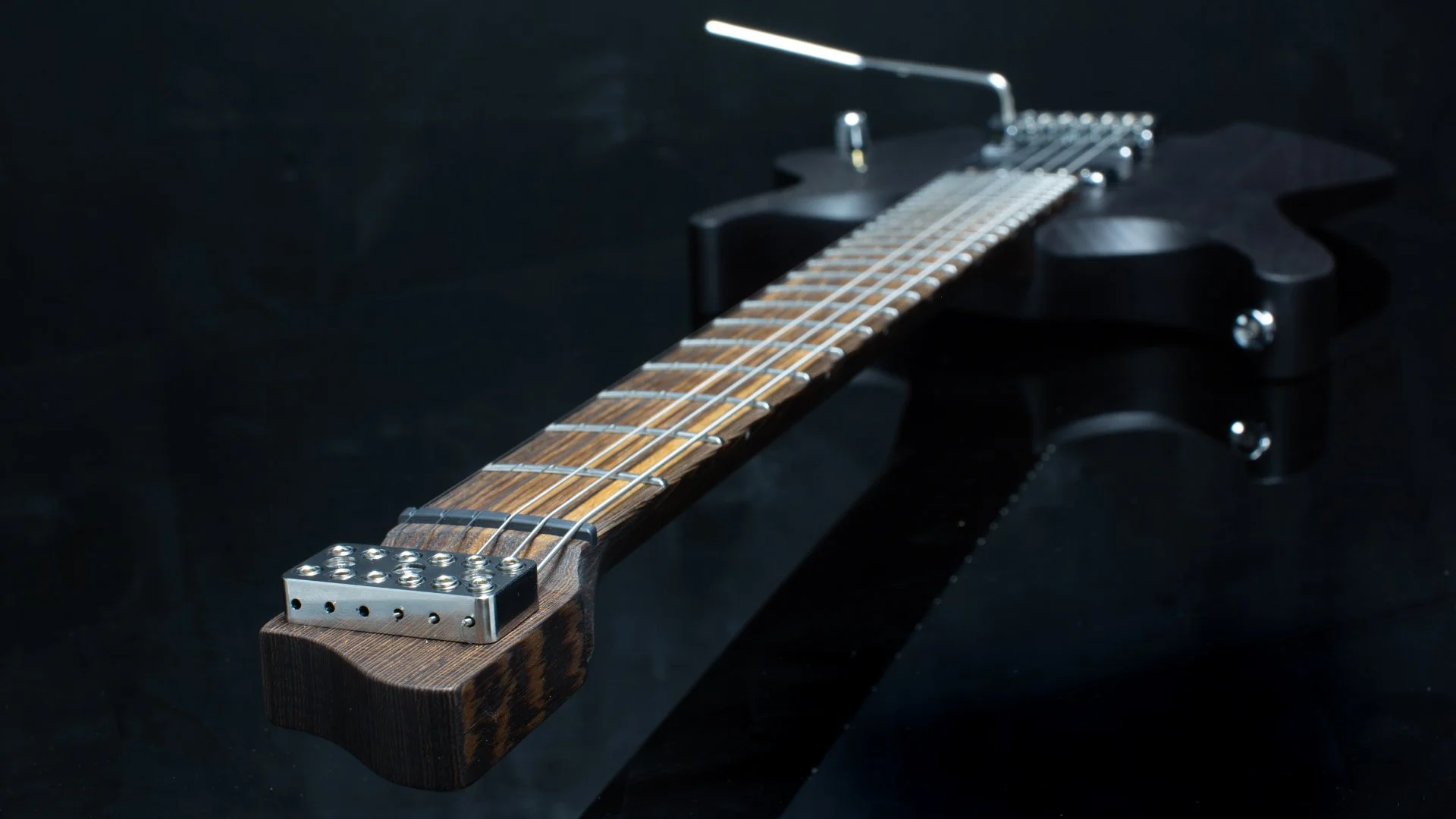 Close-up of a headless guitar with a tremolo bridge, chrome hardware against a dark background - Neck and headstock view