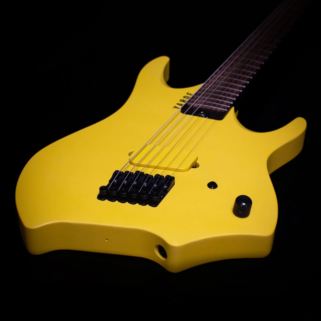 A bright yellow headless - multiscale electric guitar with a black background, featuring a custom angled wooden covered pickup and black hardware - 3/4 view of body