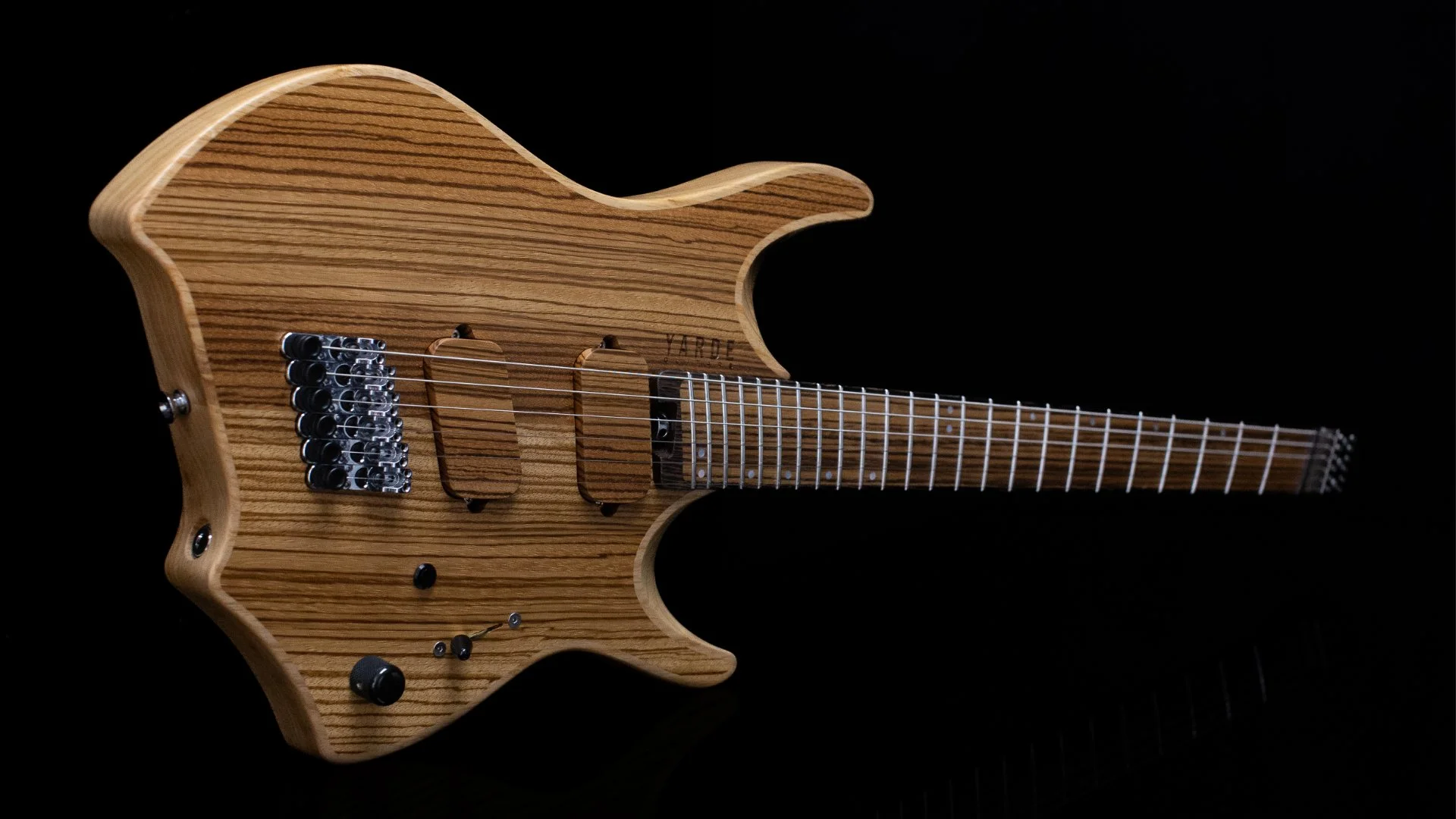 A headless - multiscale electric guitar with an inlaid cap in a natural finish, wooden pickup covers and a black background - Landscape view