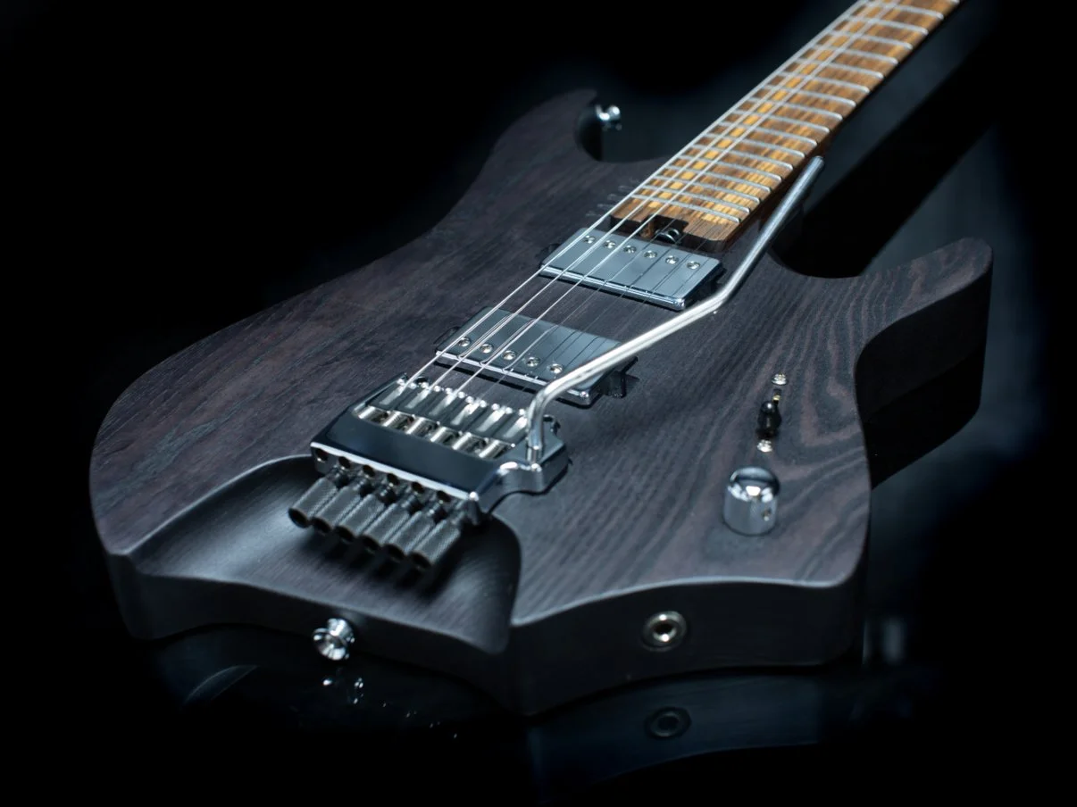 close up body view of a headless electric guitar featuring a chrome tremolo bridge and chrome covered humbuckers