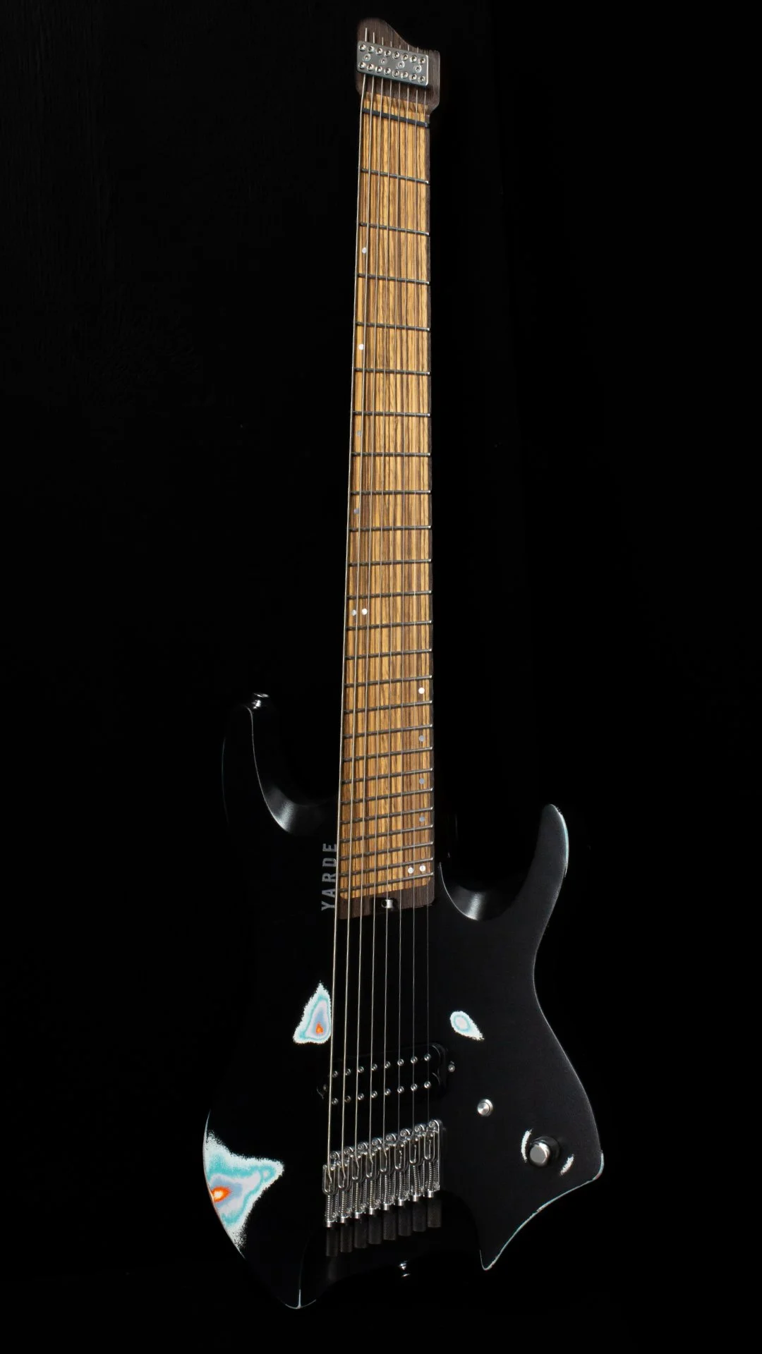 A 8 string multi coloured relic painted headless - multiscale electric guitar, one humbucker pickup, chrome hardware, Wenge neck and inlaid zebrano fretboard, against a black background - Portrait view