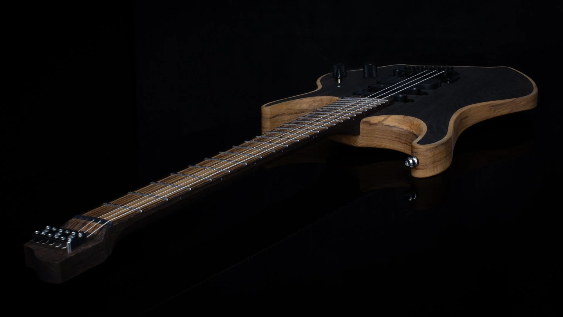 Close-up of a headless - multiscale electric guitar with an inlaid bog oak cap with a tremolo bridge against a dark background - Neck and headstock view