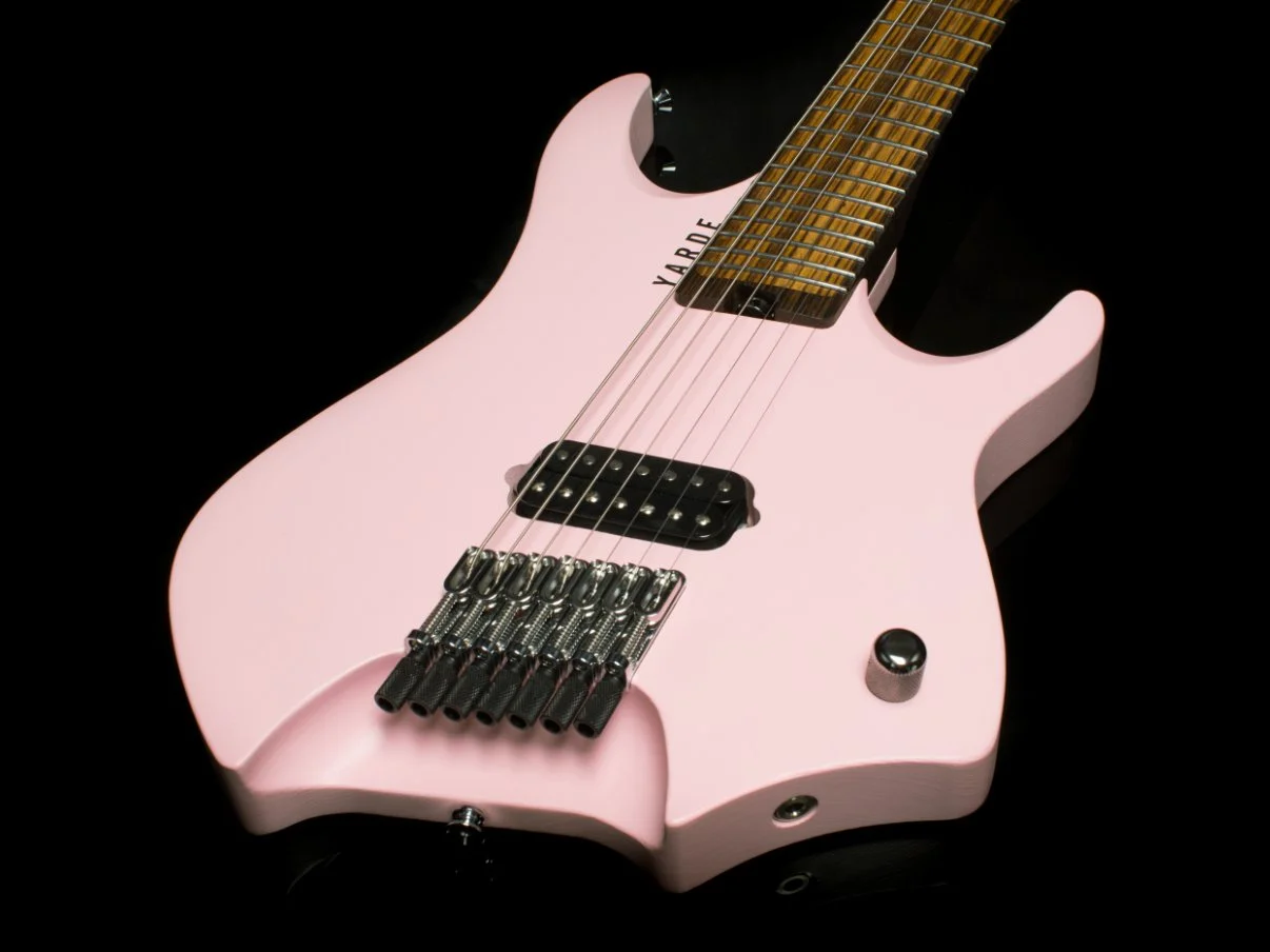 A pink headless - multiscale 7 string electric guitar with a black background, featuring an inlaid fretboard and chrome hardware - 3/4 view of body