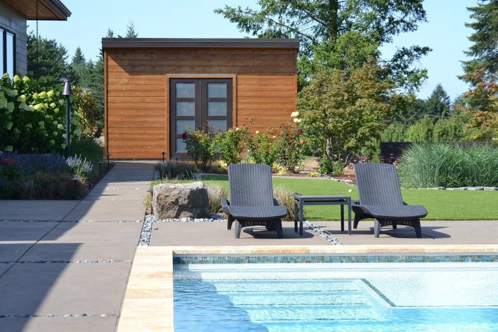 Backyard with a swimming pool, two lounge chairs, small table, garden, and a wooden shed.