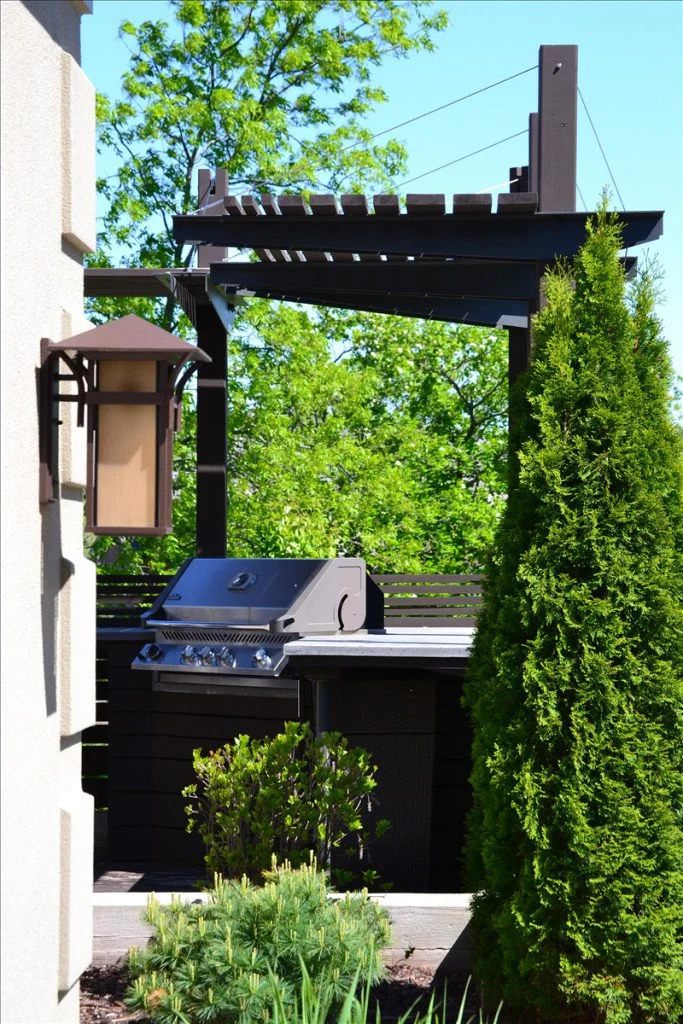Outdoor barbecue grill on a patio with greenery and a wooden pergola structure.