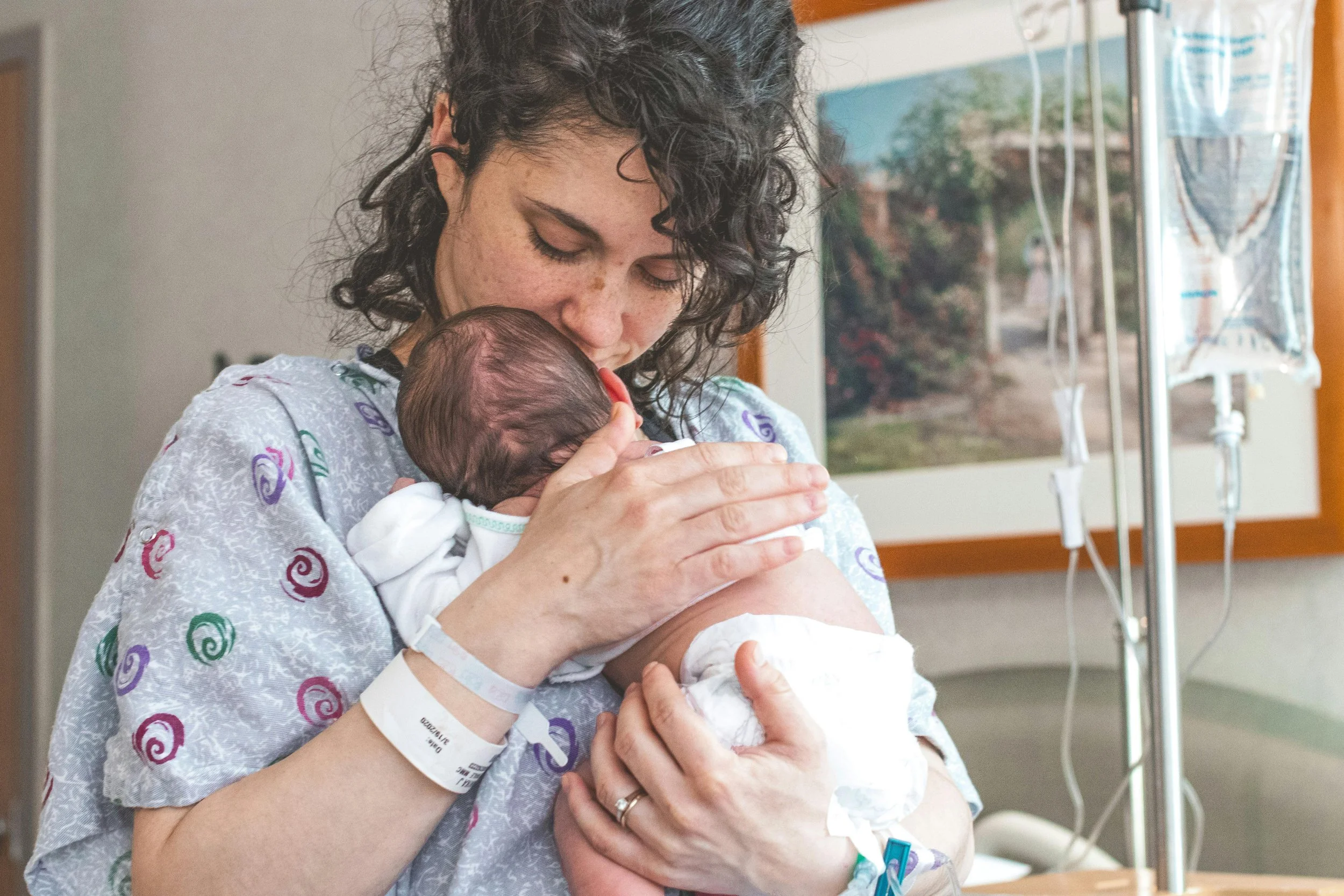 A new mother sitting by a window holding her baby, with a thoughtful and emotional expression.