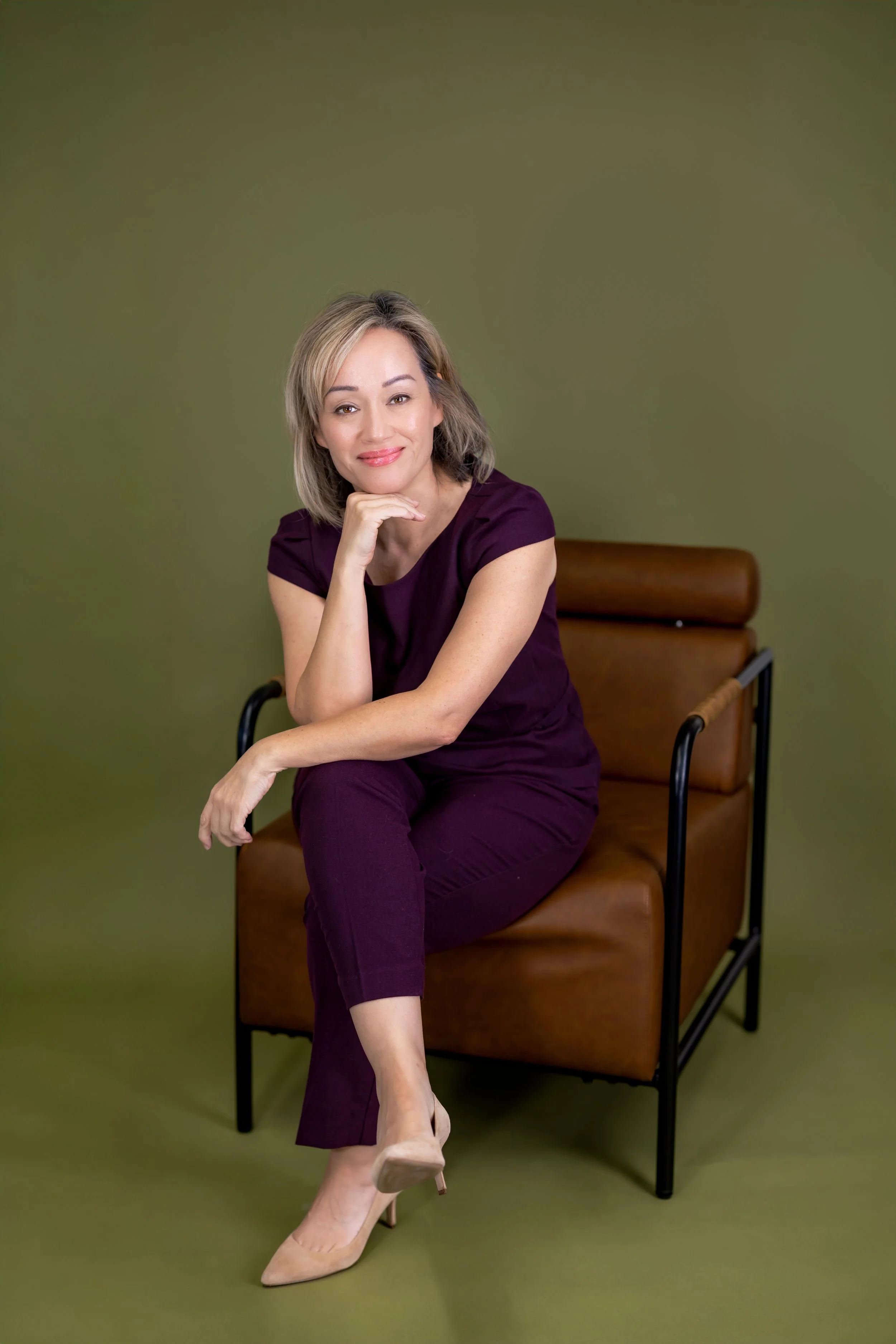 Woman seated in brown leather chair against Olive Green Savage seamless backdrop for branding photography at d14 Studio