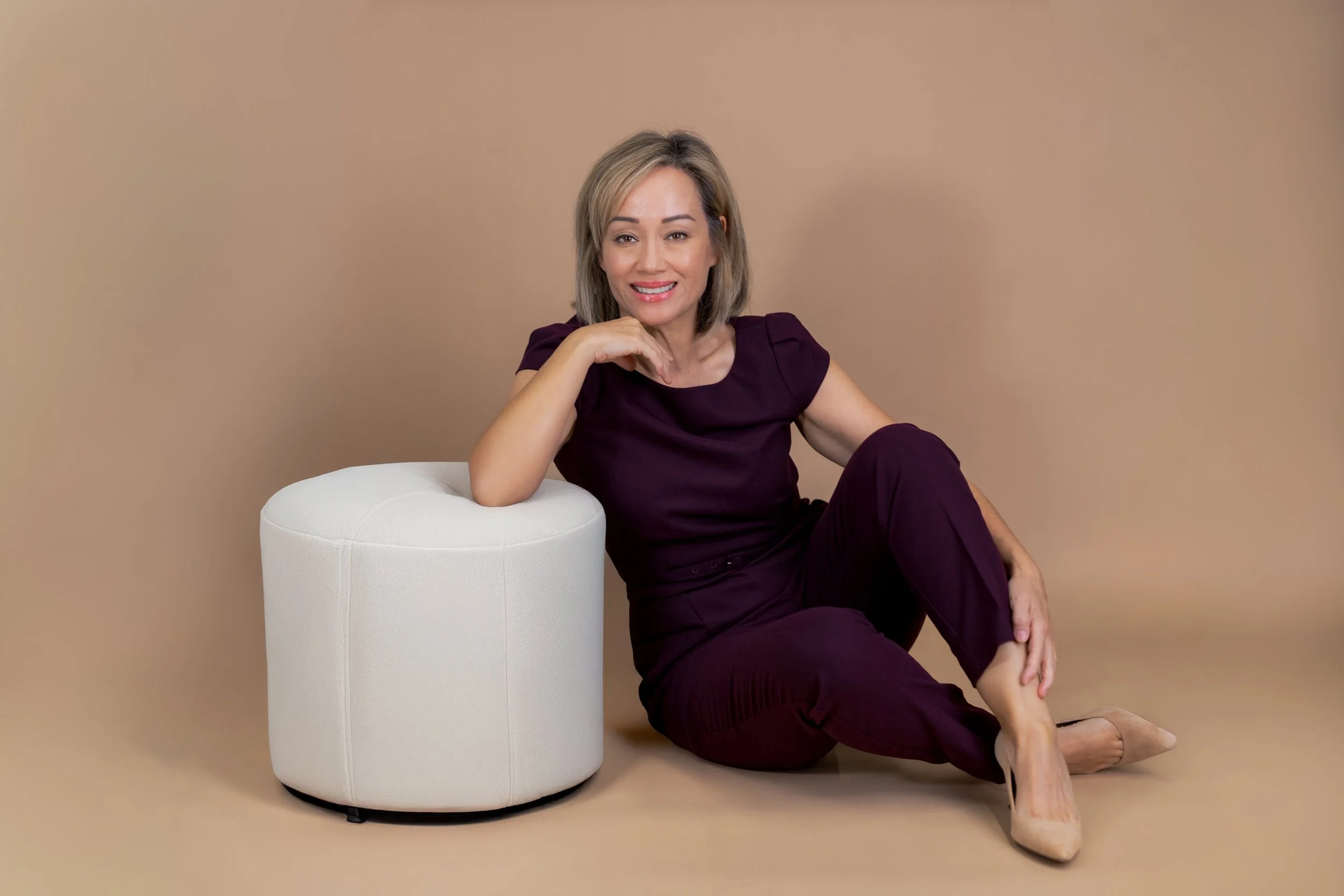 Close-up branding portrait of woman leaning on white ottoman against Beige Savage seamless backdrop