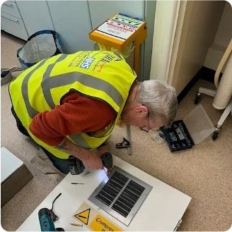 Person in a safety vest working on a metal panel with a drill