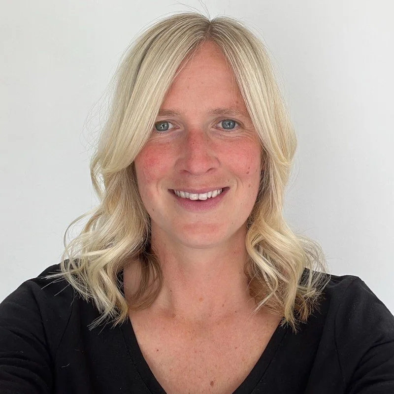 Person with blonde hair and a black shirt against a plain background.