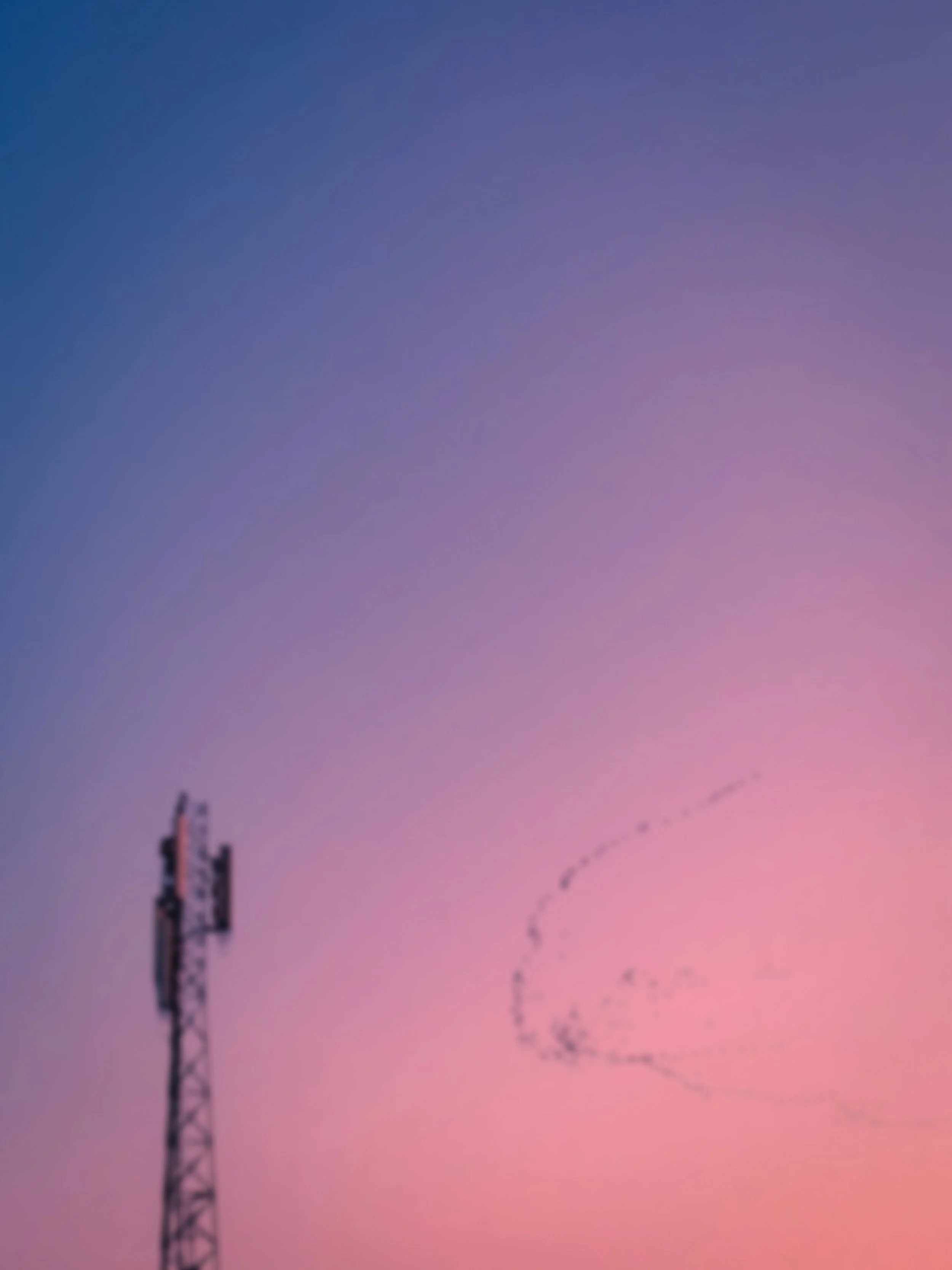 Cell tower with purple sunset sky and distant flock of birds flying.
