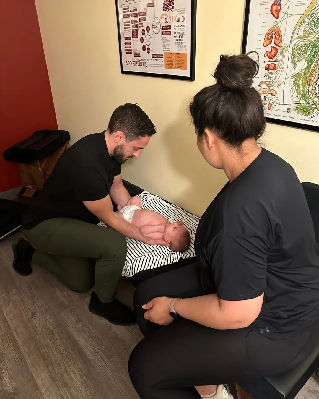 chiropractor checking a baby's spine while cradling in his arms in front of mom patient