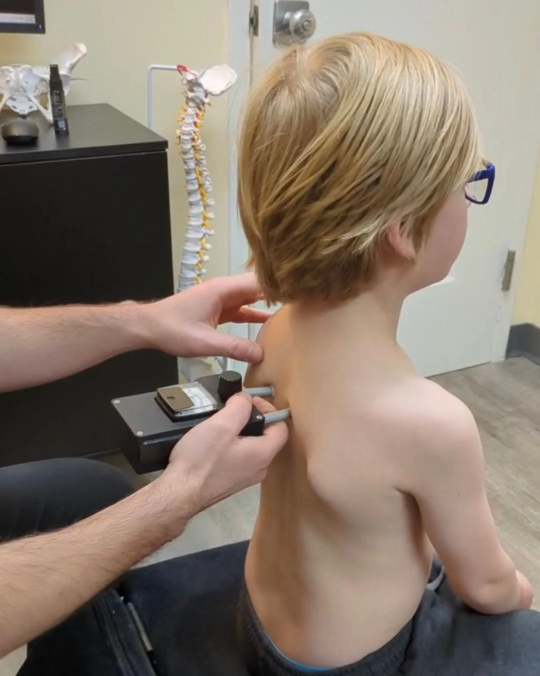 young blonde boy with glasses having his spine examined with a nervoscope