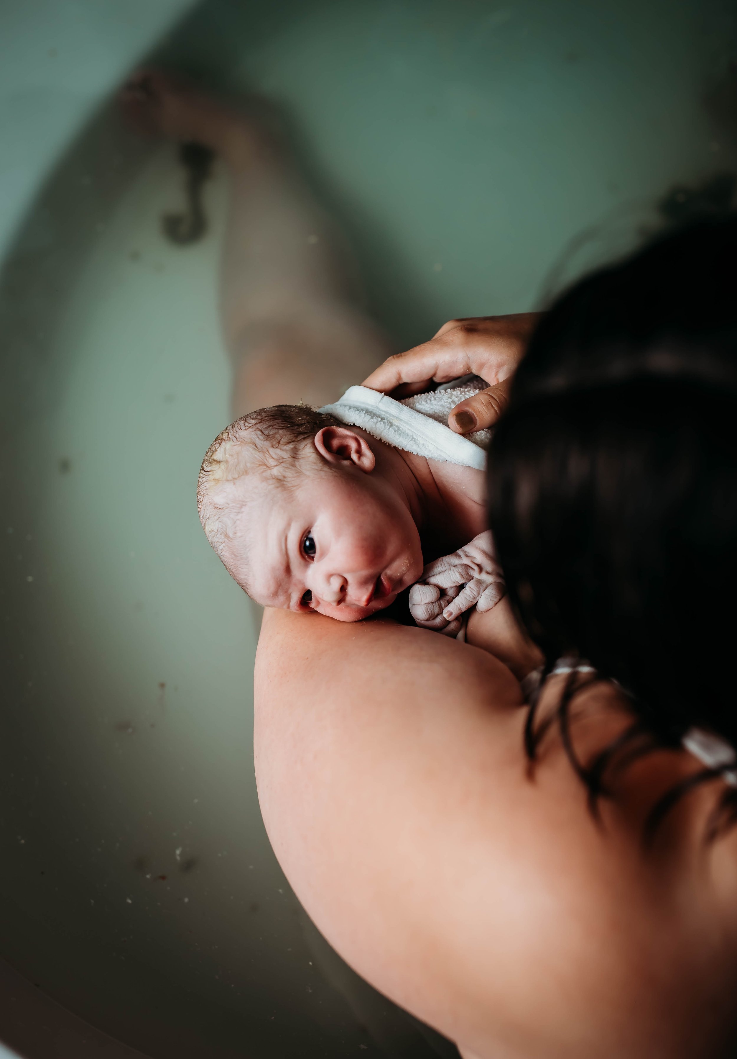 Newborn baby in mother's arms in a bathtub.