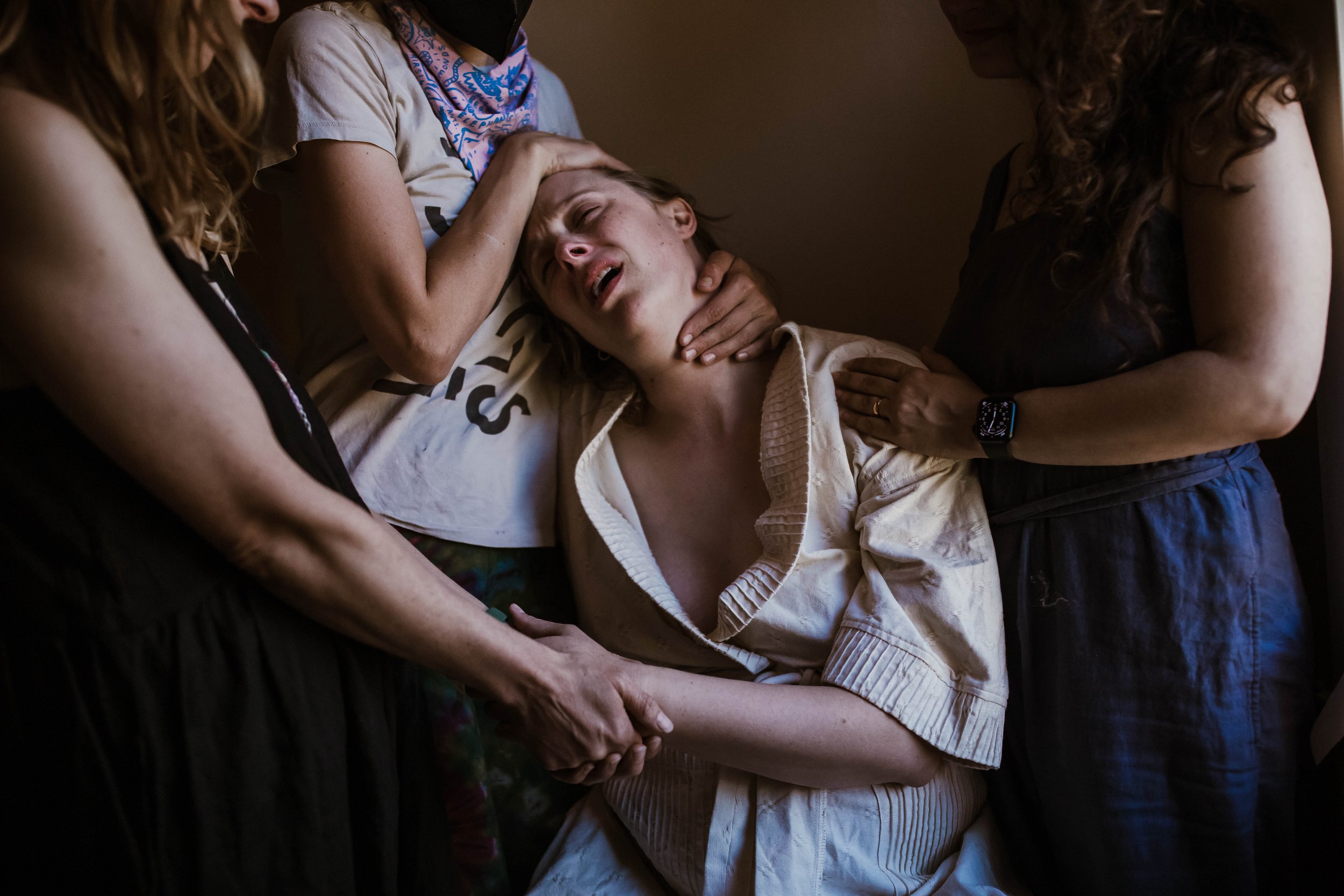 A woman in labor supported by three people providing comfort and assistance.