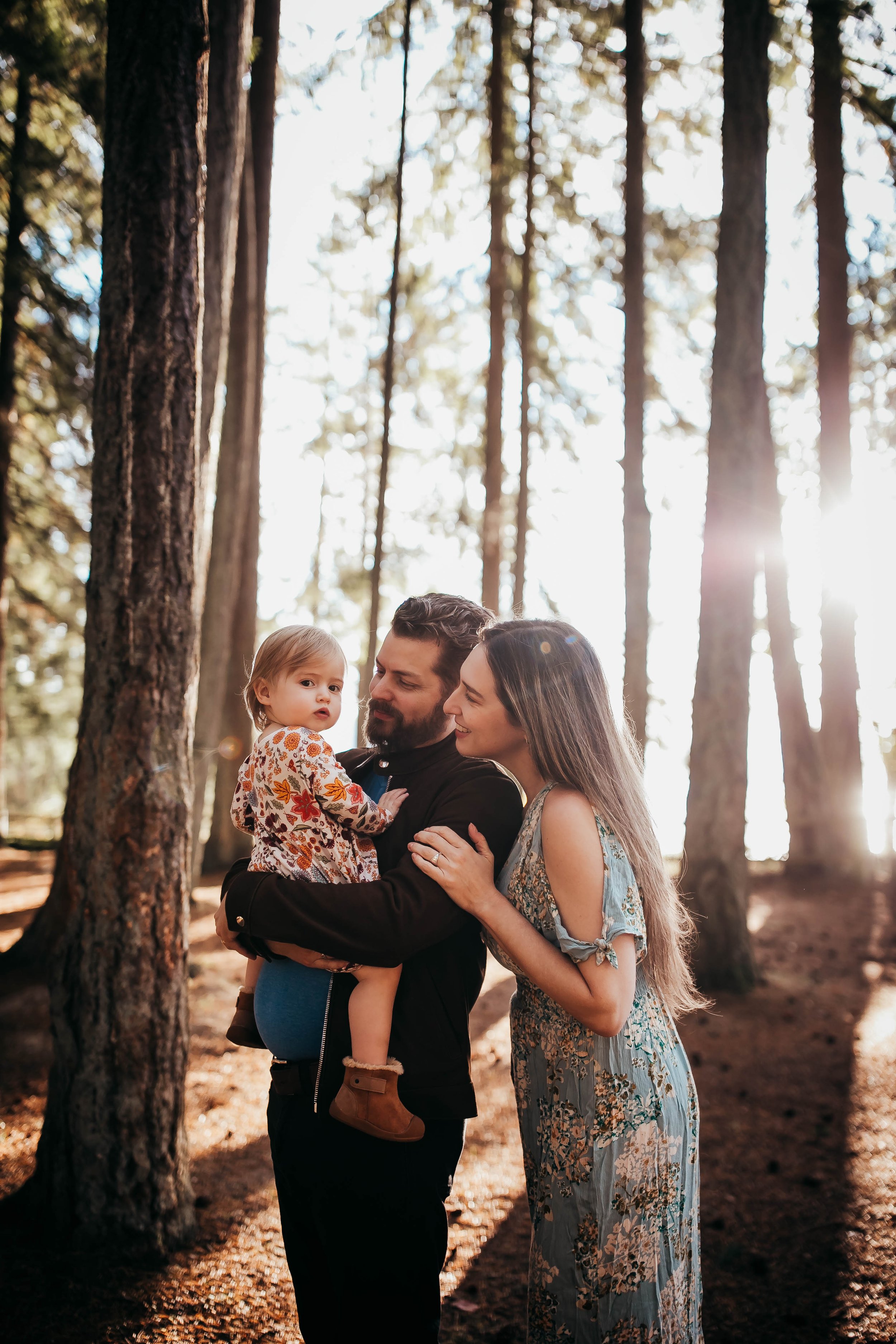 Family with a child in a forest surrounded by tall trees, sunlight filtering through the branches.