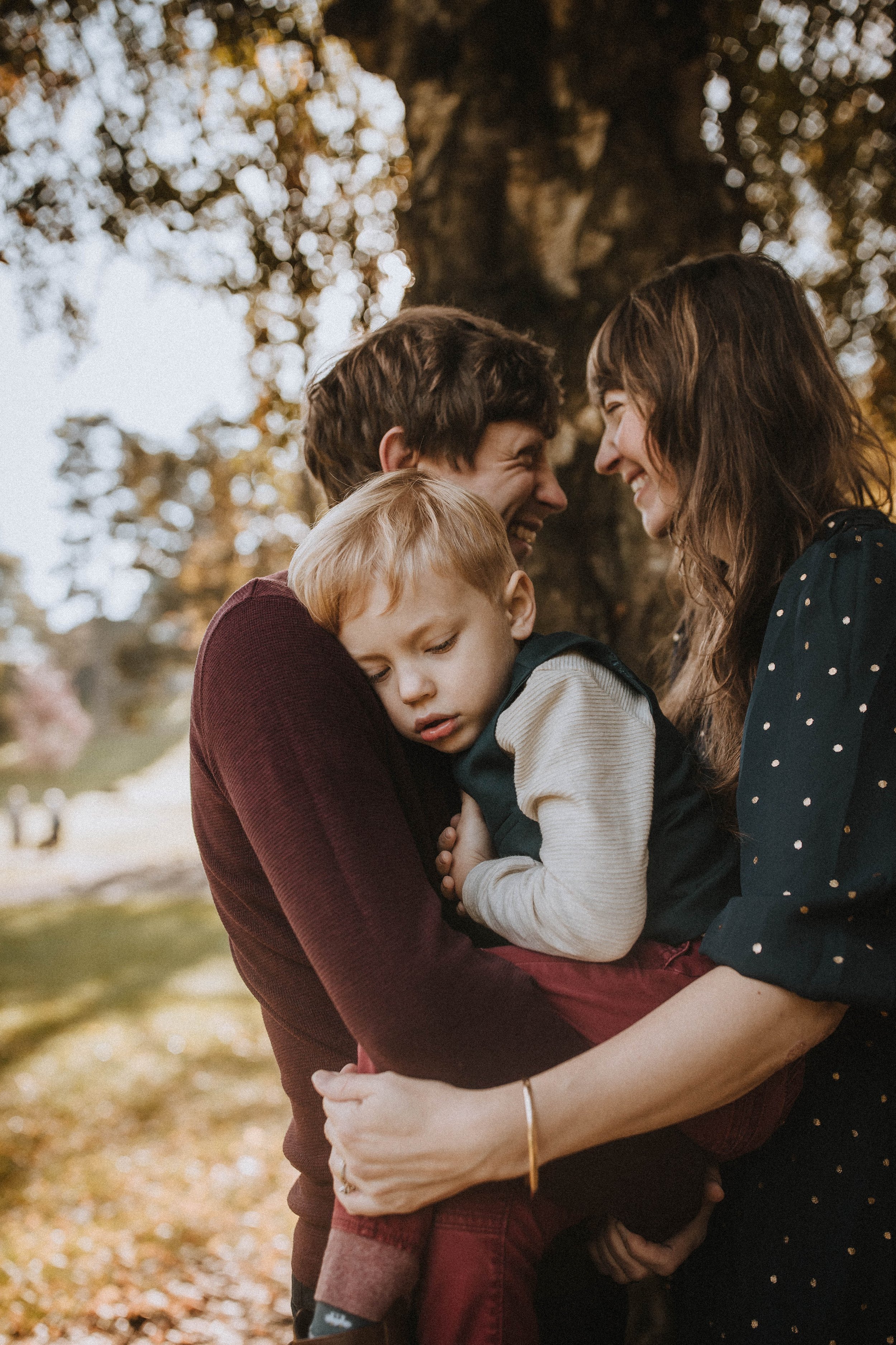 A couple standing outdoors, holding a sleeping child in their arms.