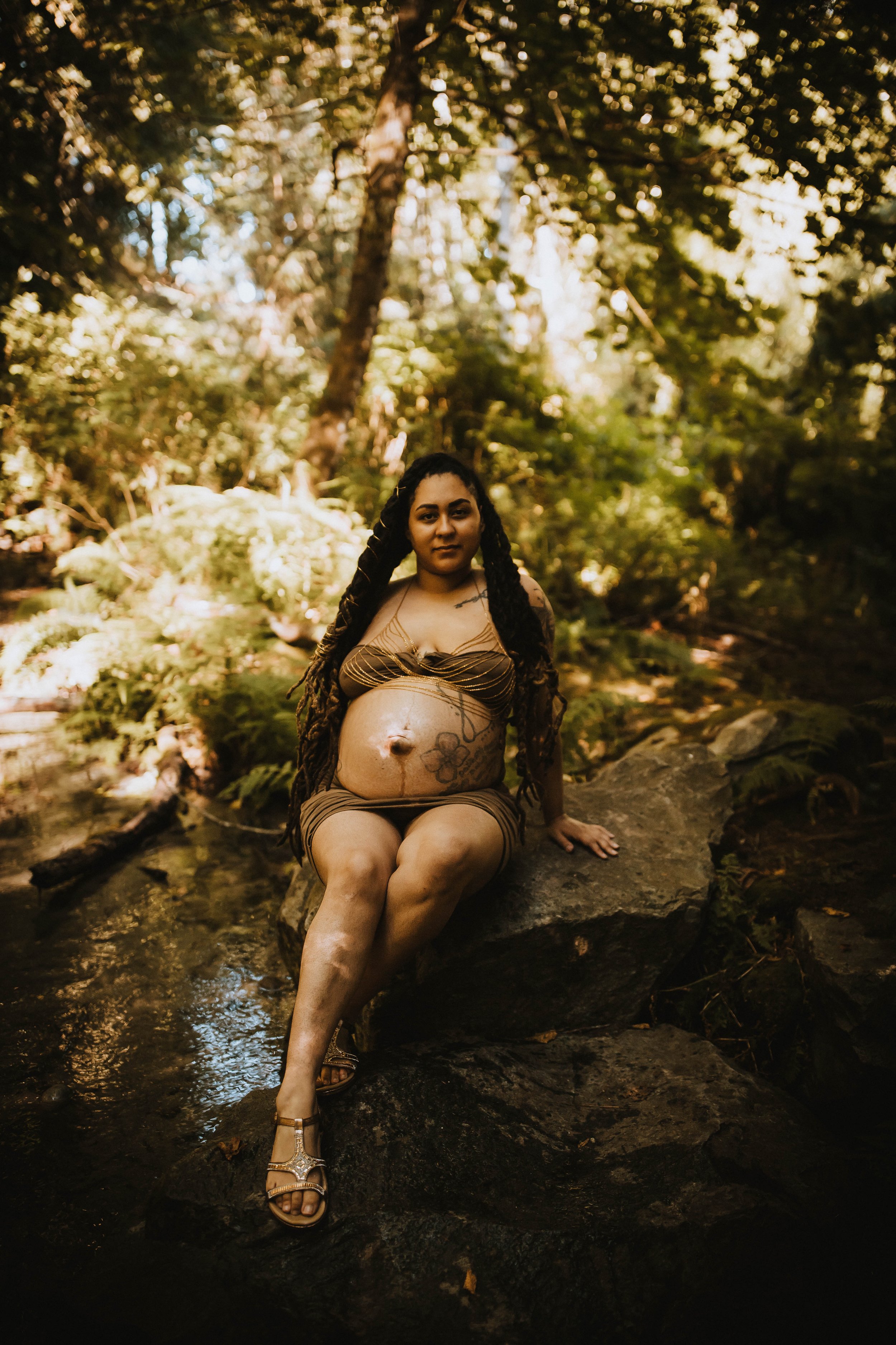 Pregnant woman sitting on rock in forest