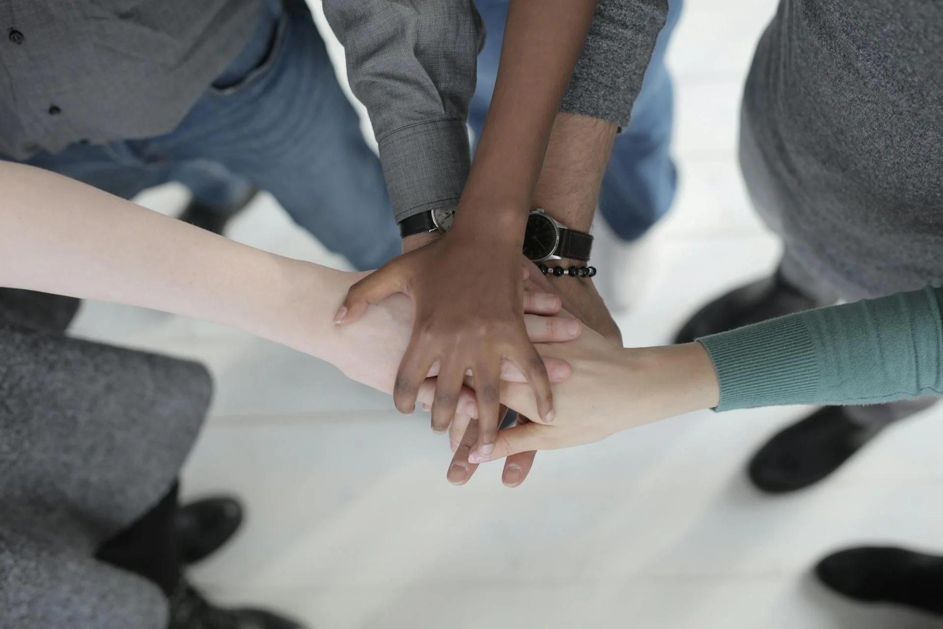 Five hands of diverse skin tones clasped together in unison