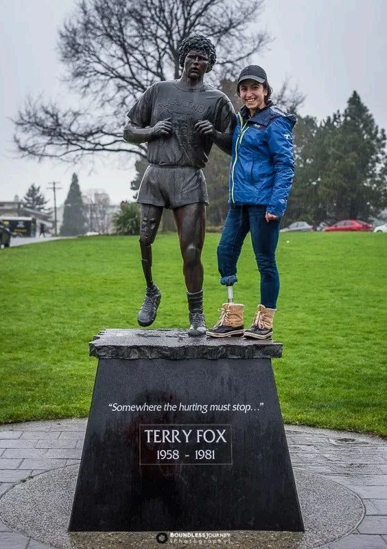 A lower limb female amputee standing next to a bronze statue of Terry Fox