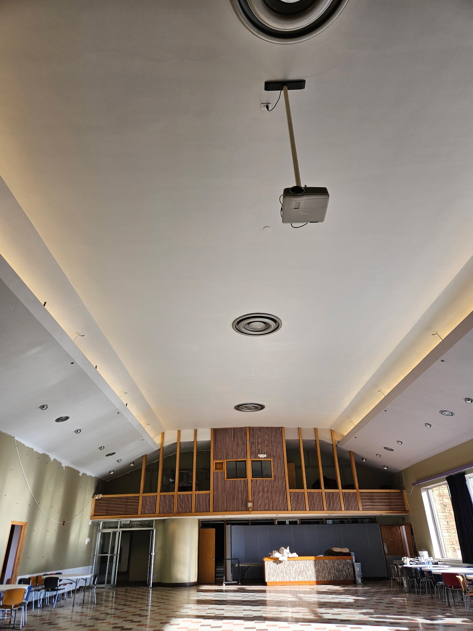 Interior Painting at a church in progress a ceiling shot of a large white ceiling with wood architectural details on the back wall of a fellowship area with a few tables and chairs