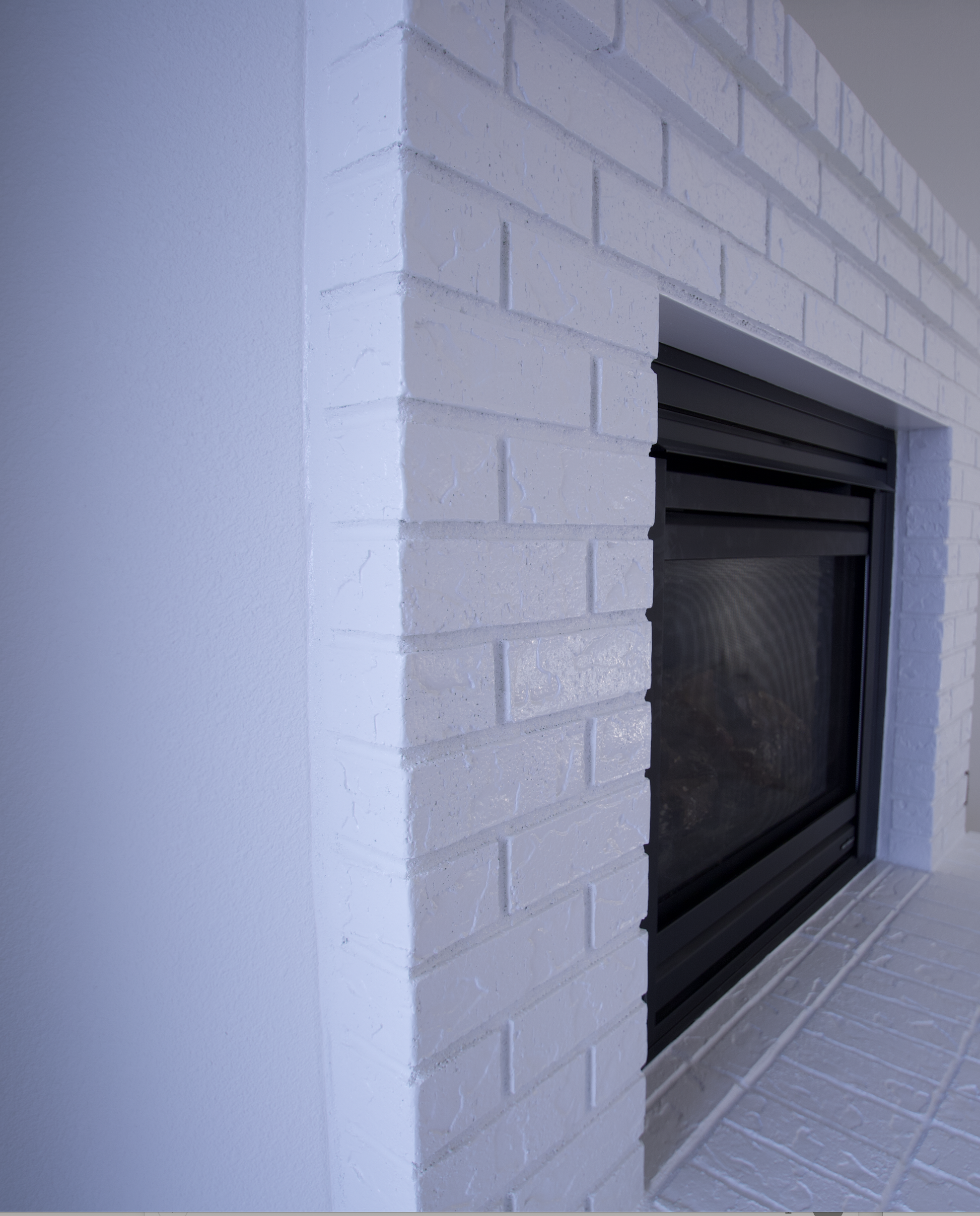 side angle of brick fireplace painted shiny white with black metal insert shot from an interesting angle