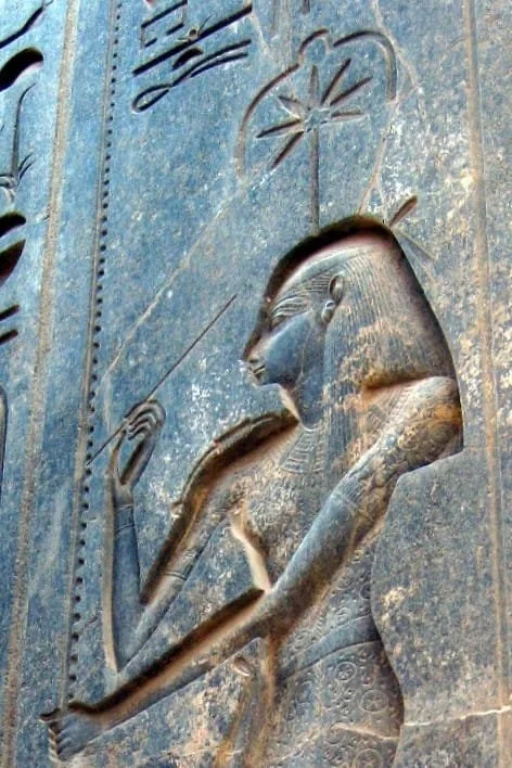 Ancient Egyptian carved relief showing the goddess Seshat with a headdress, holding a staff, with hieroglyphic symbols of a seven-pointed star above her.