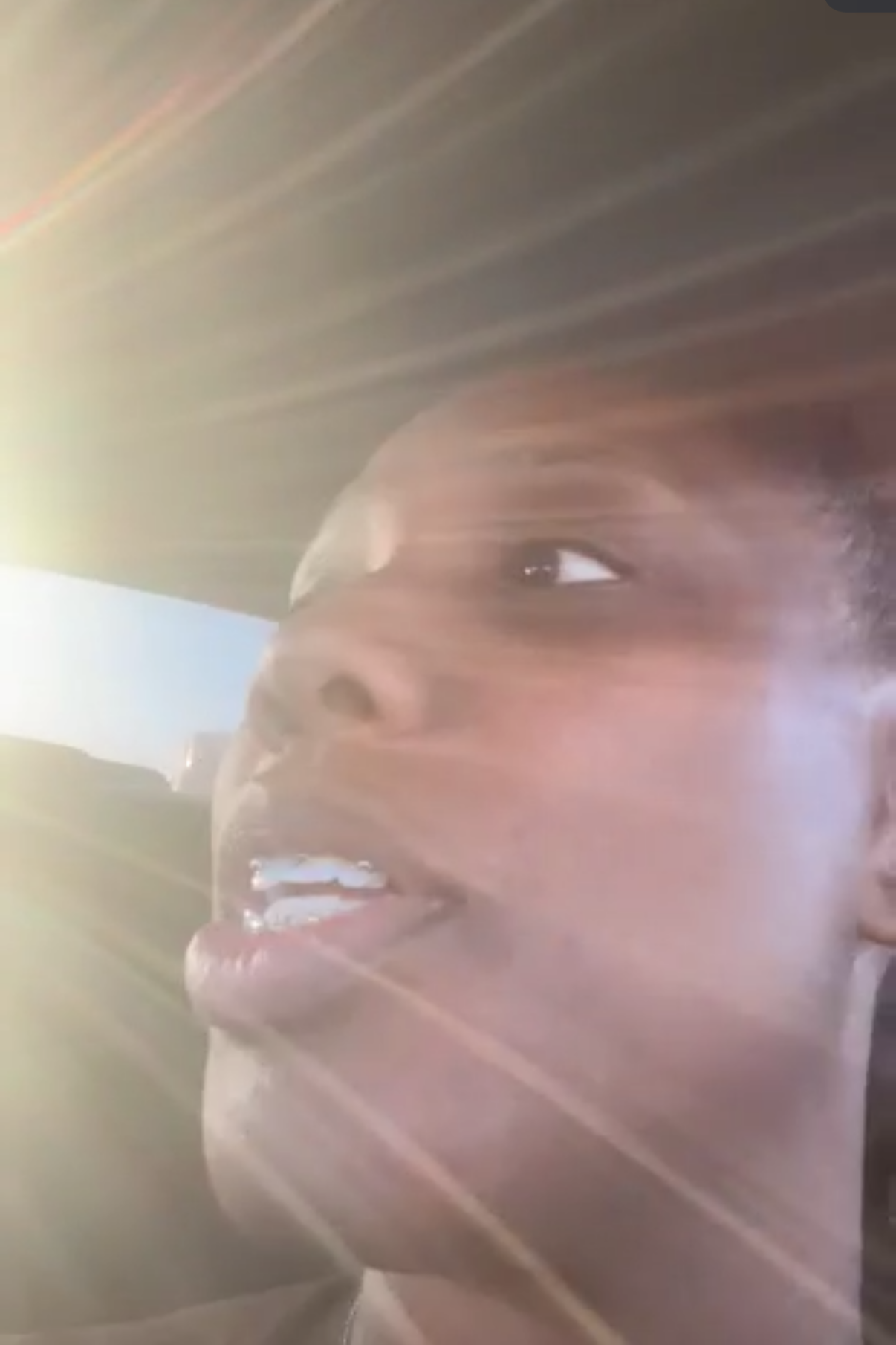 Close-up of a smiling young woman with long hair, illuminated by bright sunlight with lens flare.