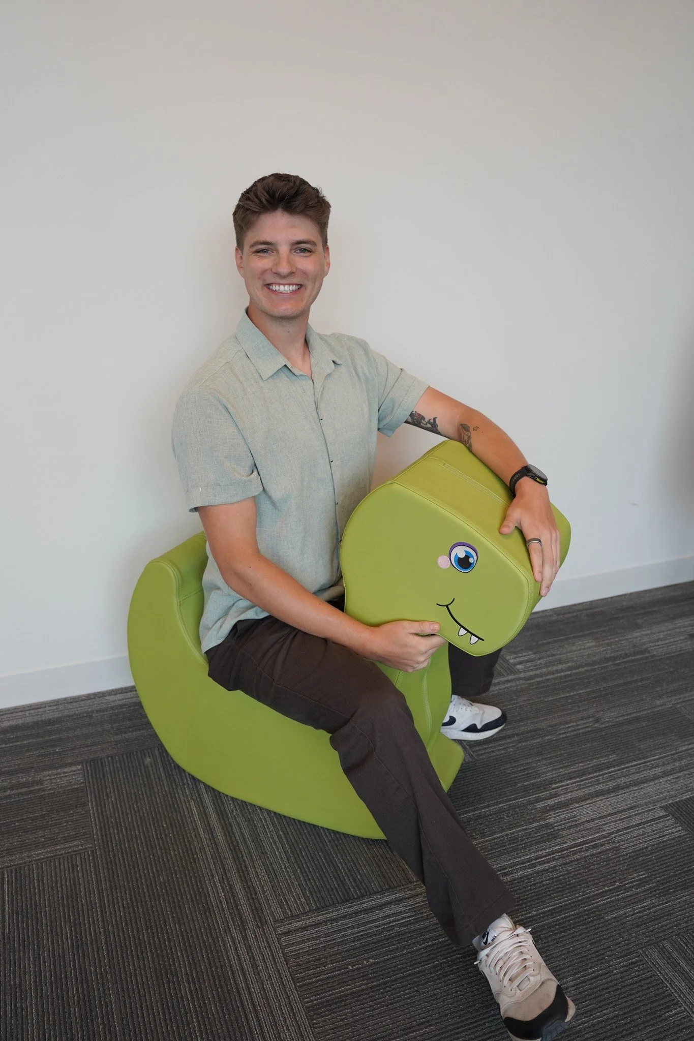 Regional sales manager Luke Diller sits on a green foam dinosaur and smiles. 