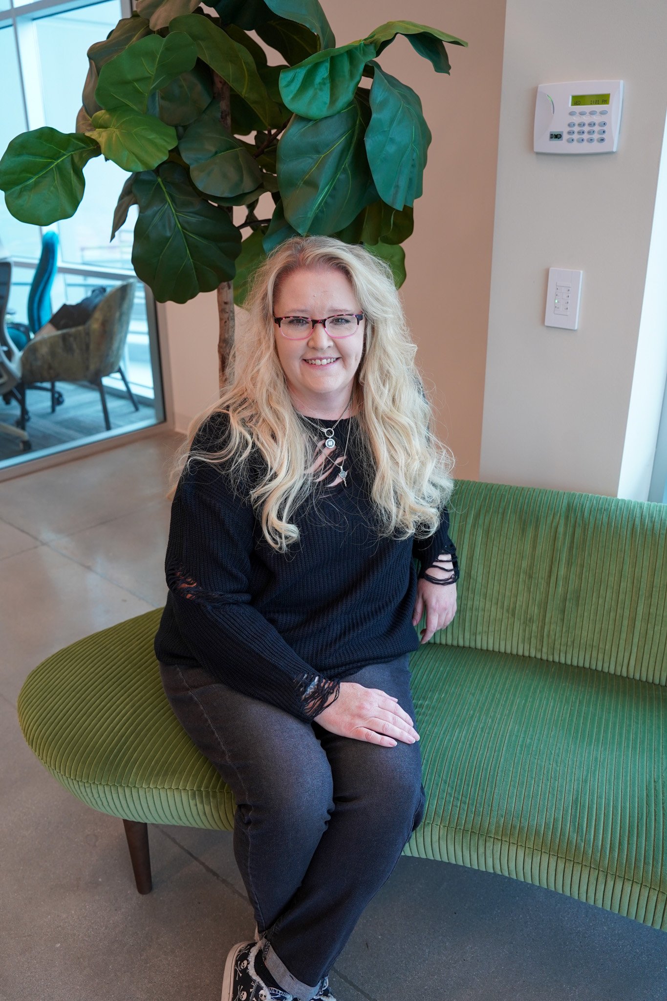 Kim Smith, bookkeeping, has hair down and is wearing a black shirt and blue pants while she sits and smiles. 