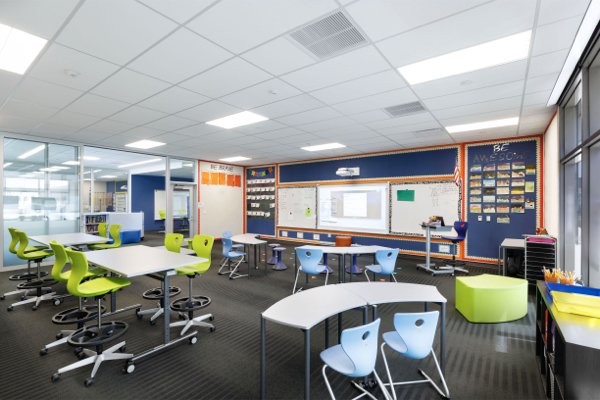 A classroom filled with white desks, green and blue chairs for students. 