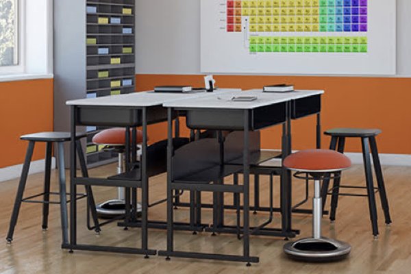 A classroom with orange walls and two tables that form one larger table. Stools with orange fabric surround the tables. 