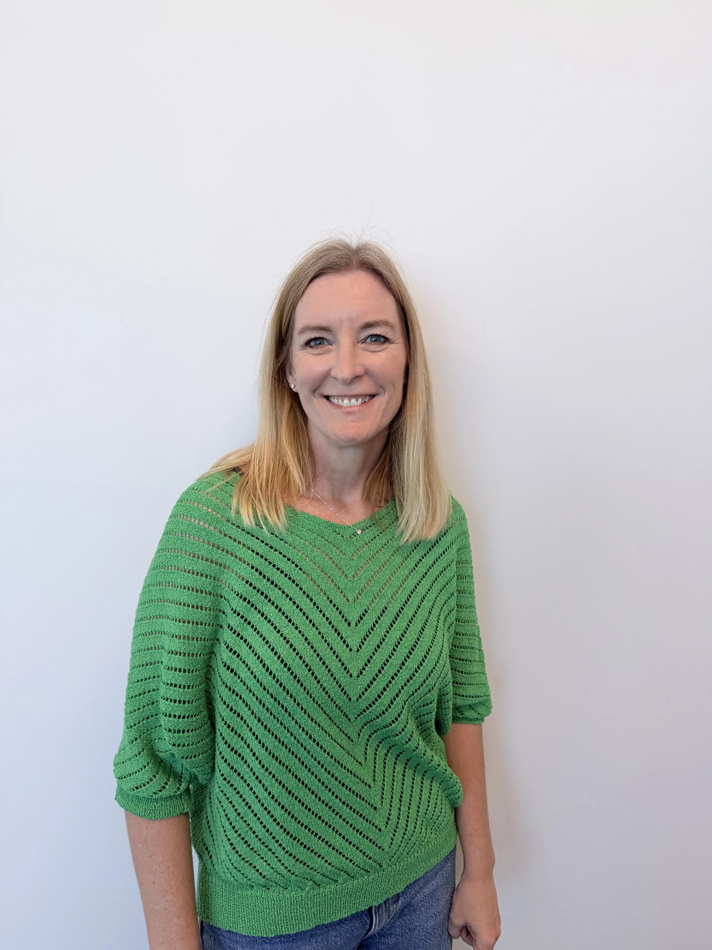 Regional sales manager Tara Carlson stands in front of a white wall wearing a green crochet top.