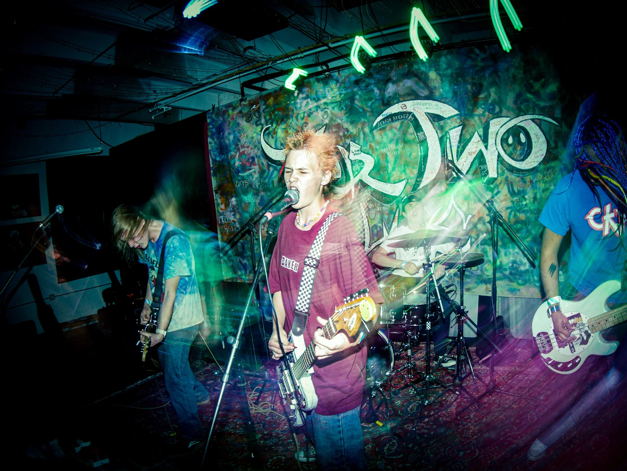 A punk rock band playing in front of a graffitied Tier Two Live banner at the Youth Battle of the Bands