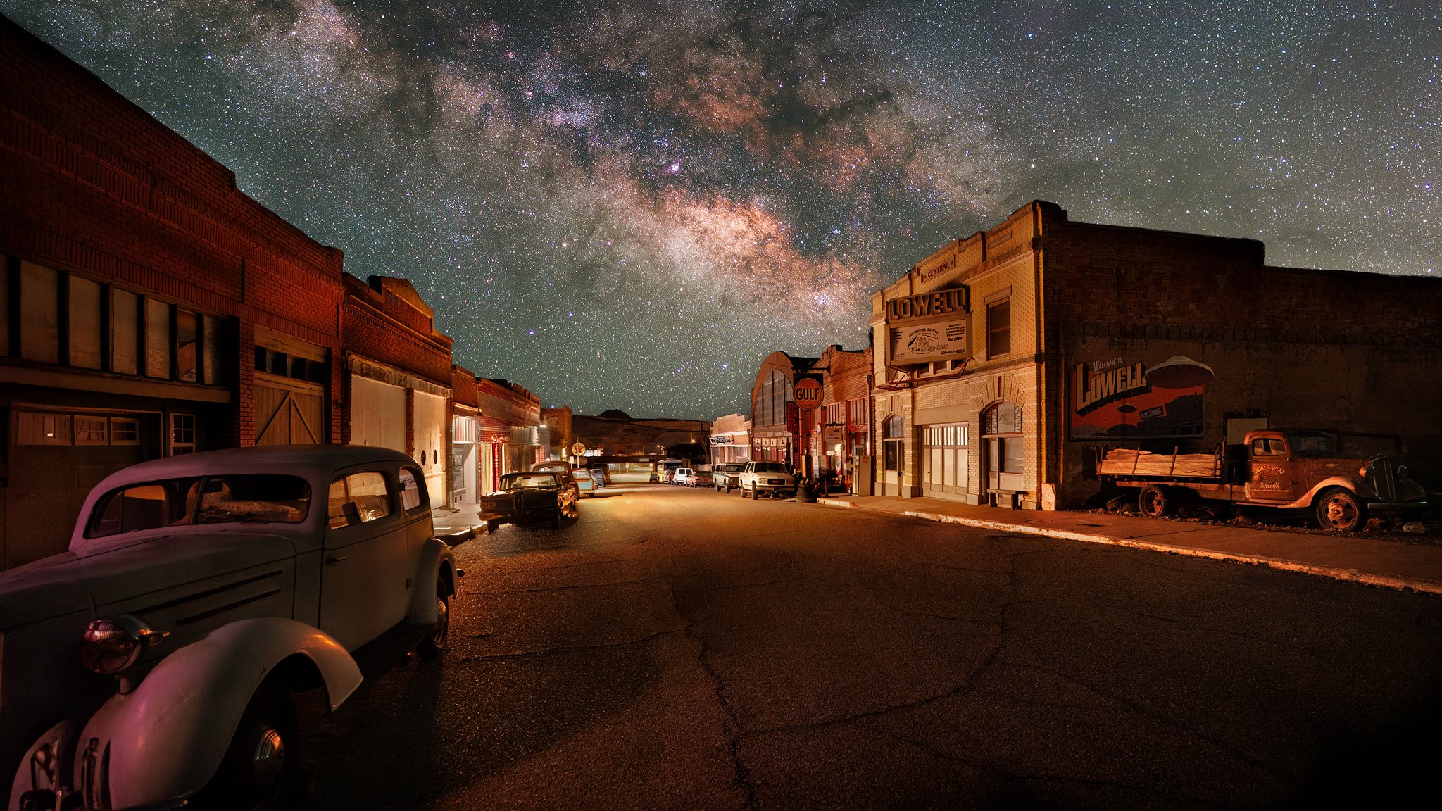 Historic Erie Street in Lowell with vintage storefronts, Gulf gas station, and classic cars under brilliant Milky Way arch