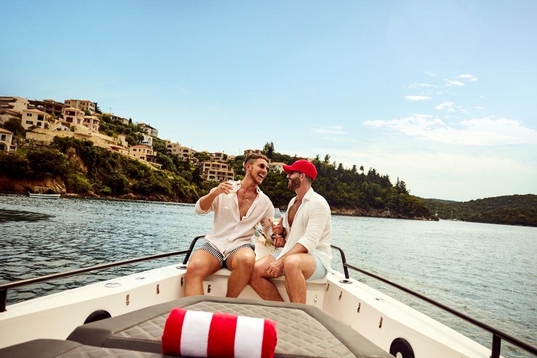 Two men relaxing on a boat along a green Mediterranean coastline