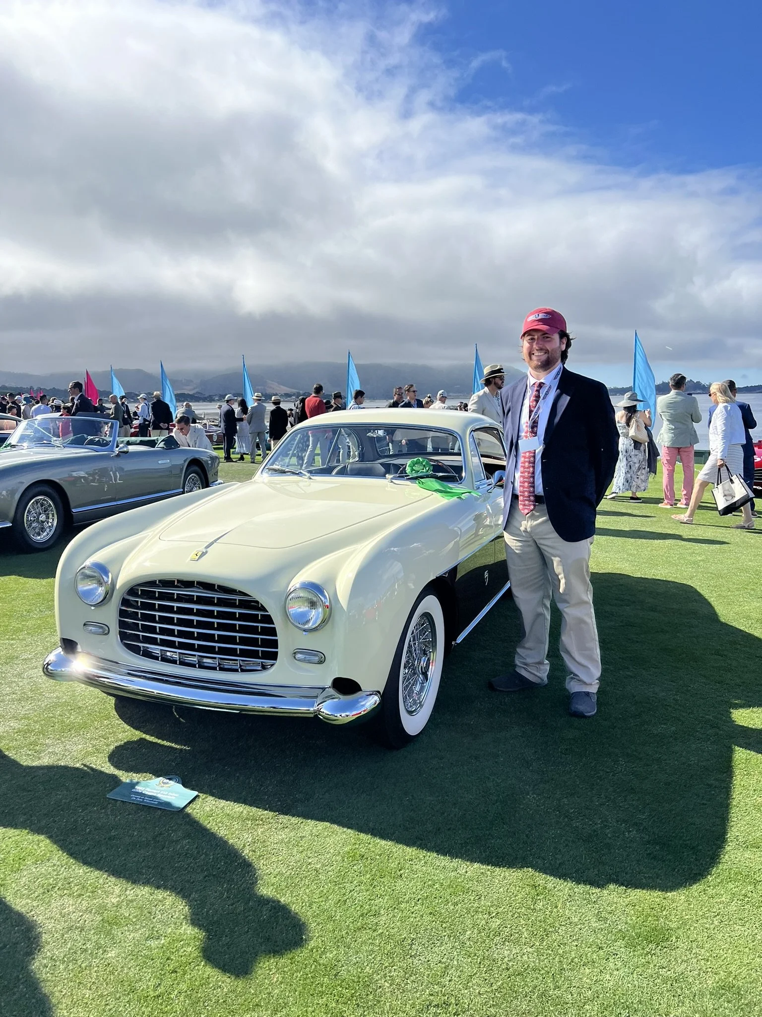 Lucas Aubrey Picard, in a dark blazer, light-colored pants, and a red cap, stands next to a 1952 Ferrari 212 Inter Ghia Coupe (s/n 0191EL) at the Pebble Beach Concours d’Elegance.
