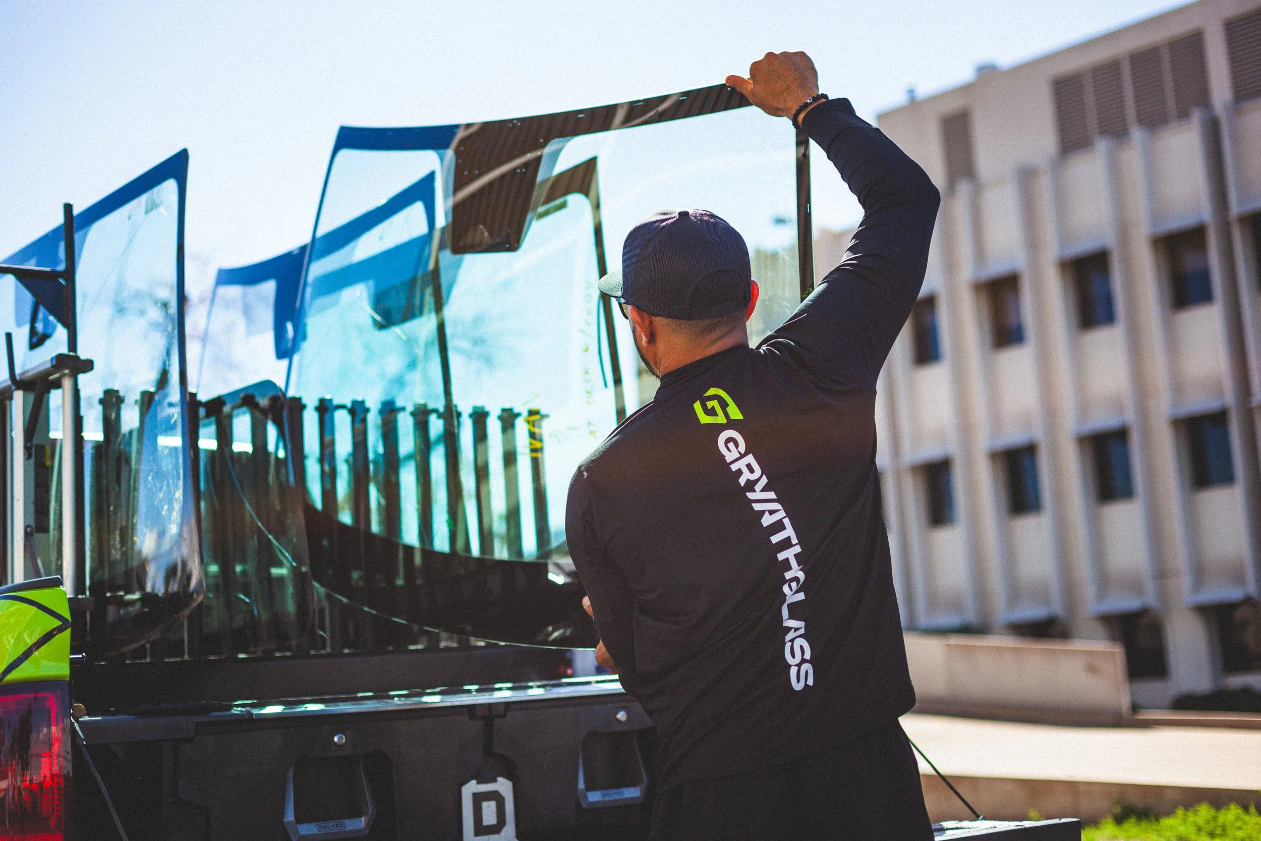 An auto glass technician in a black shirt loads glass panels onto a truck equipped with a secure rack system in an urban setting.