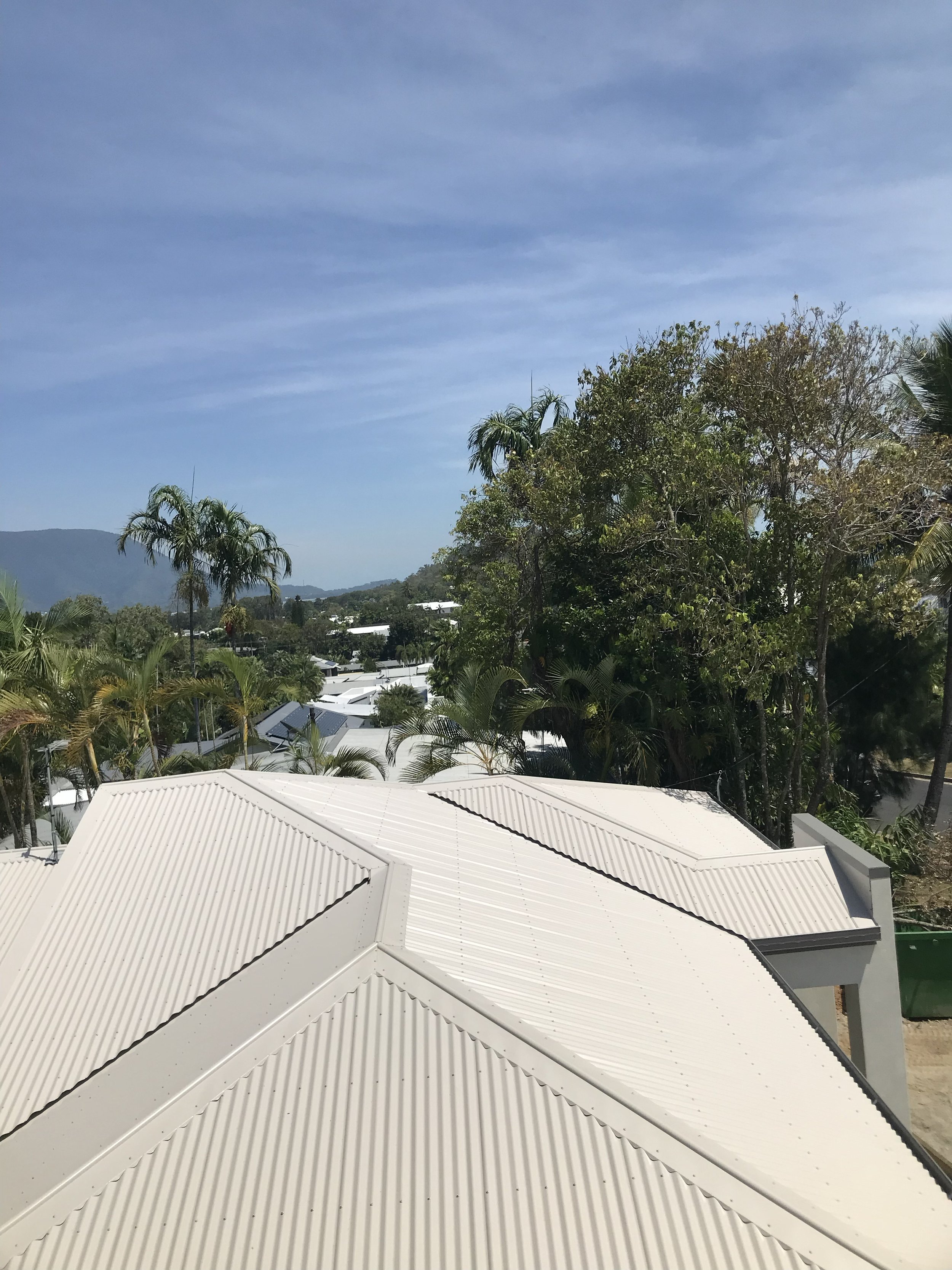View of white metal rooftops with lush green trees and a clear blue sky in the background.