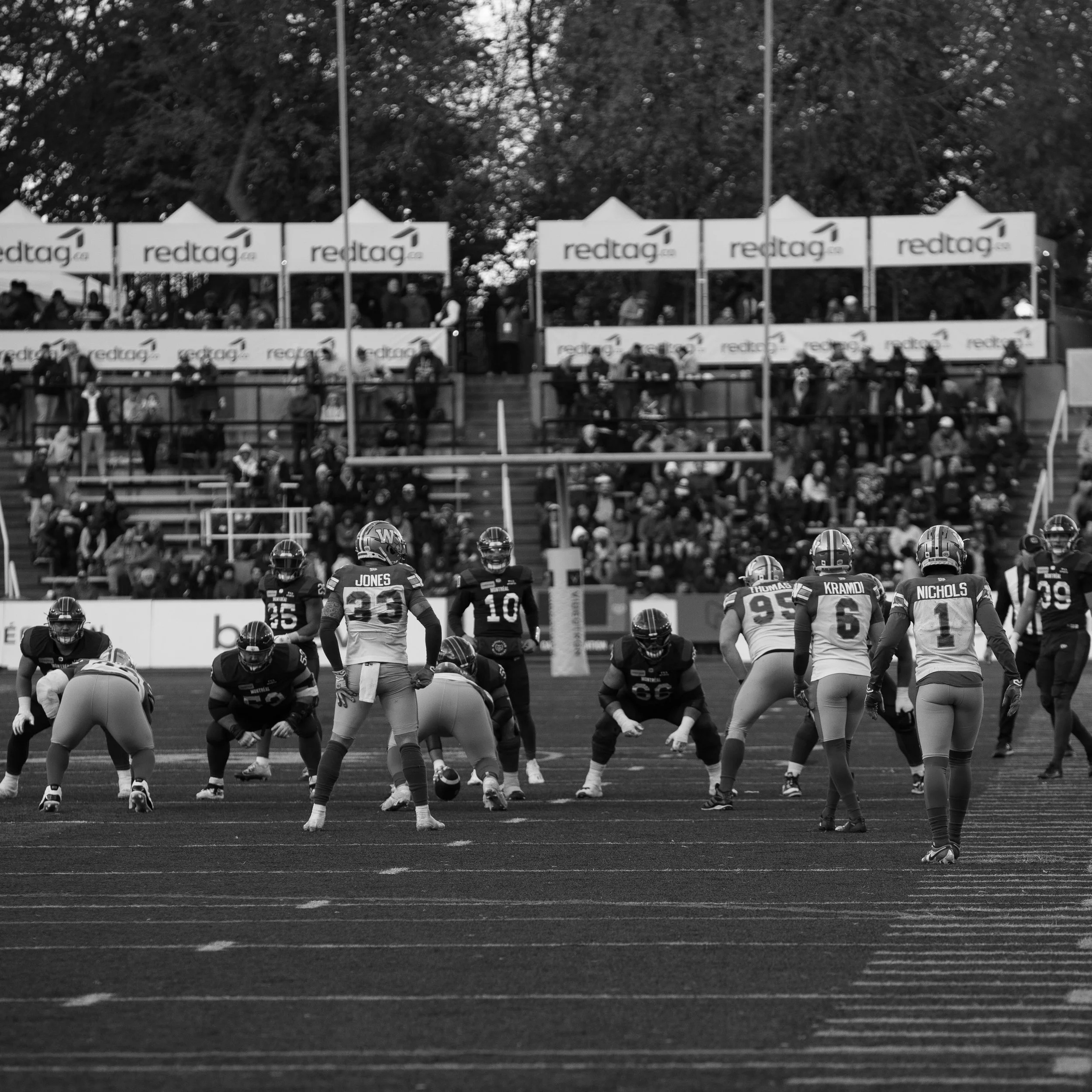Une scène de match de football américain avec des joueurs alignés sur le terrain et un public dans les gradins en arrière-plan.