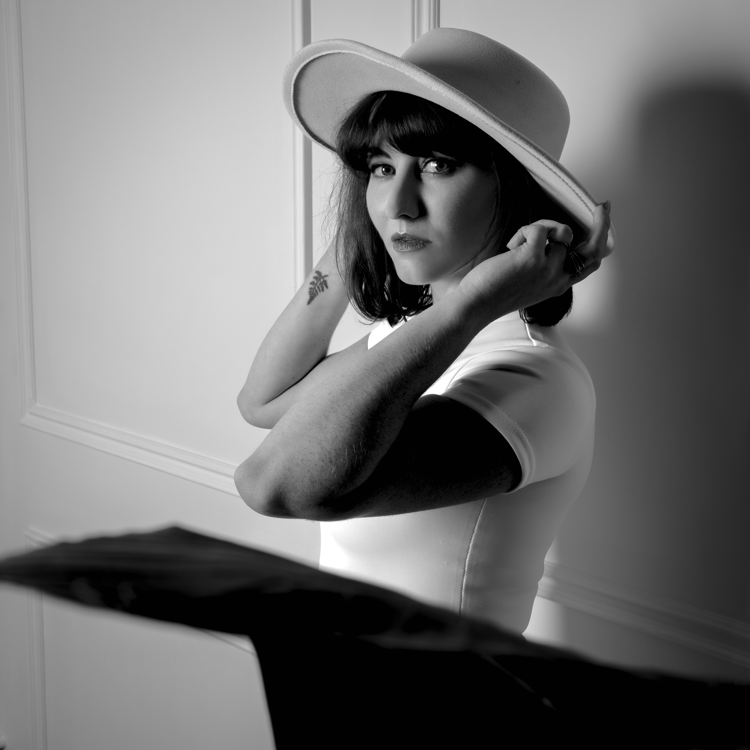 Une femme portant un chapeau large et un t-shirt blanc, regardant l'objectif, dans une image en noir et blanc