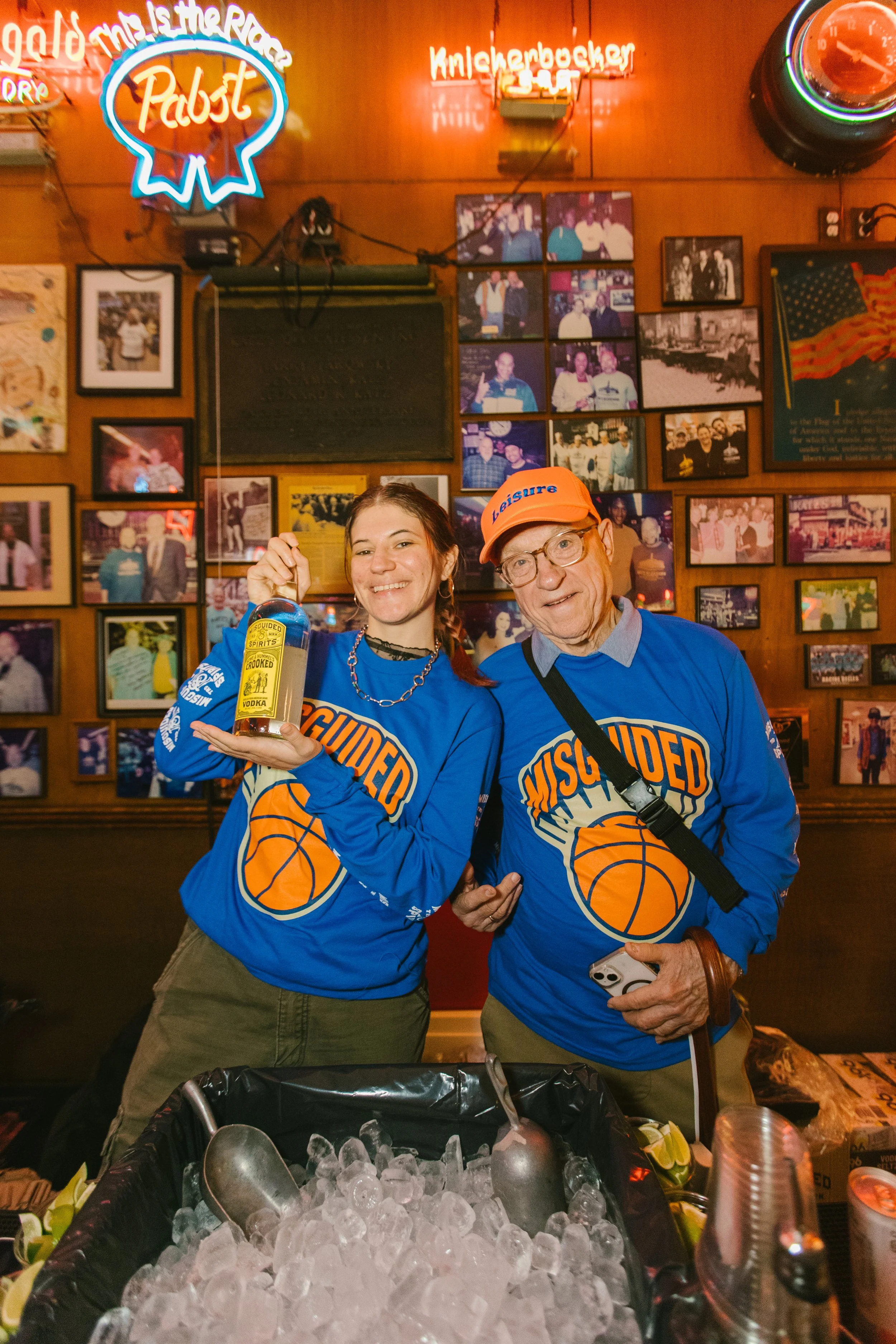 michael and geena in Misguided Knicks shirts posing in front of the iconic celebrity wall at Katz's Deli in New york city