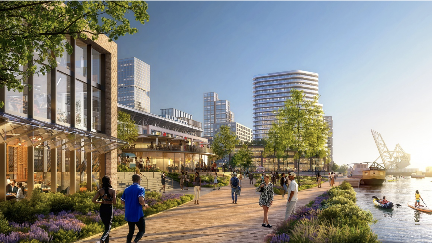 Urban waterfront promenade with modern buildings, trees, people walking, and boats on the water, during sunset.
