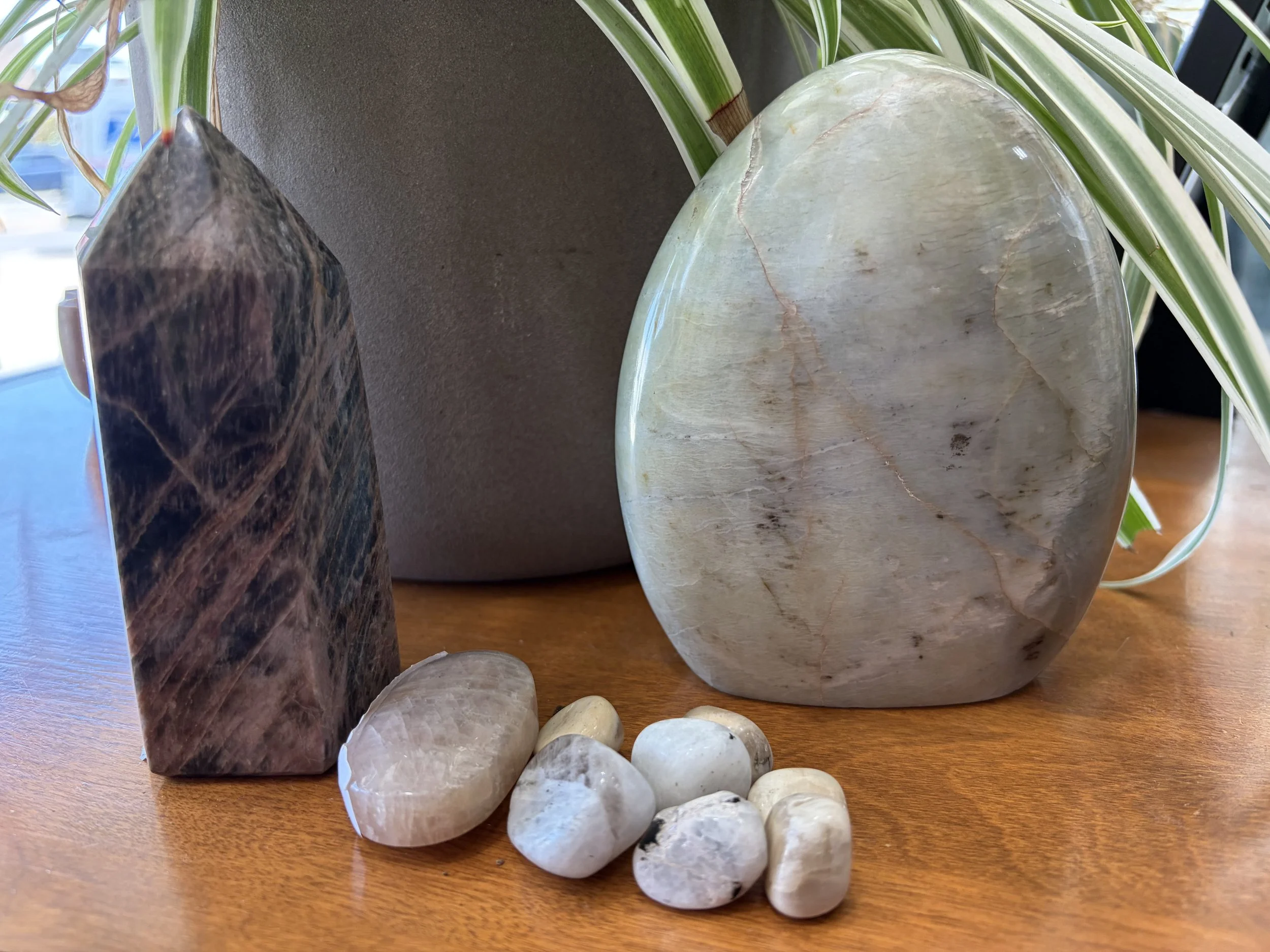 Various small polished gemstones and a central clear quartz crystal on a dark surface