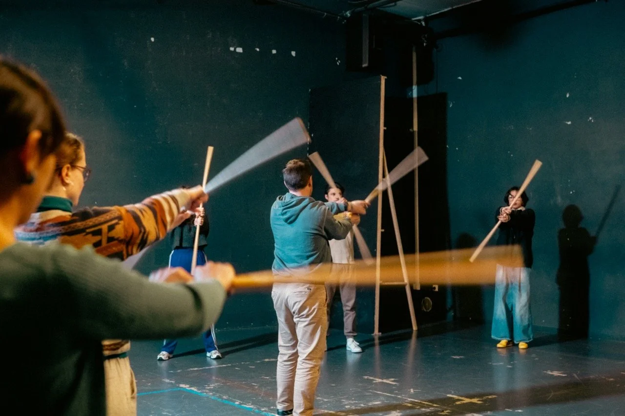 Groupe de personnes pratiquant le systema avec des bâtons en bois dans une salle de répétition.