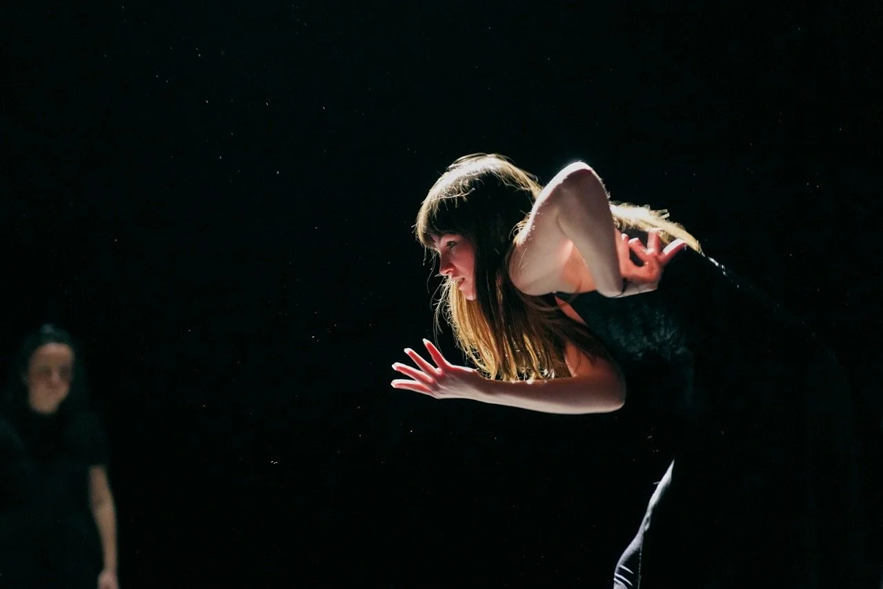 Une élève de la formation de l'acteur et de l'actrice sur scène, penchée en avant, en pleine performance théâtrale, avec un fond noir.
