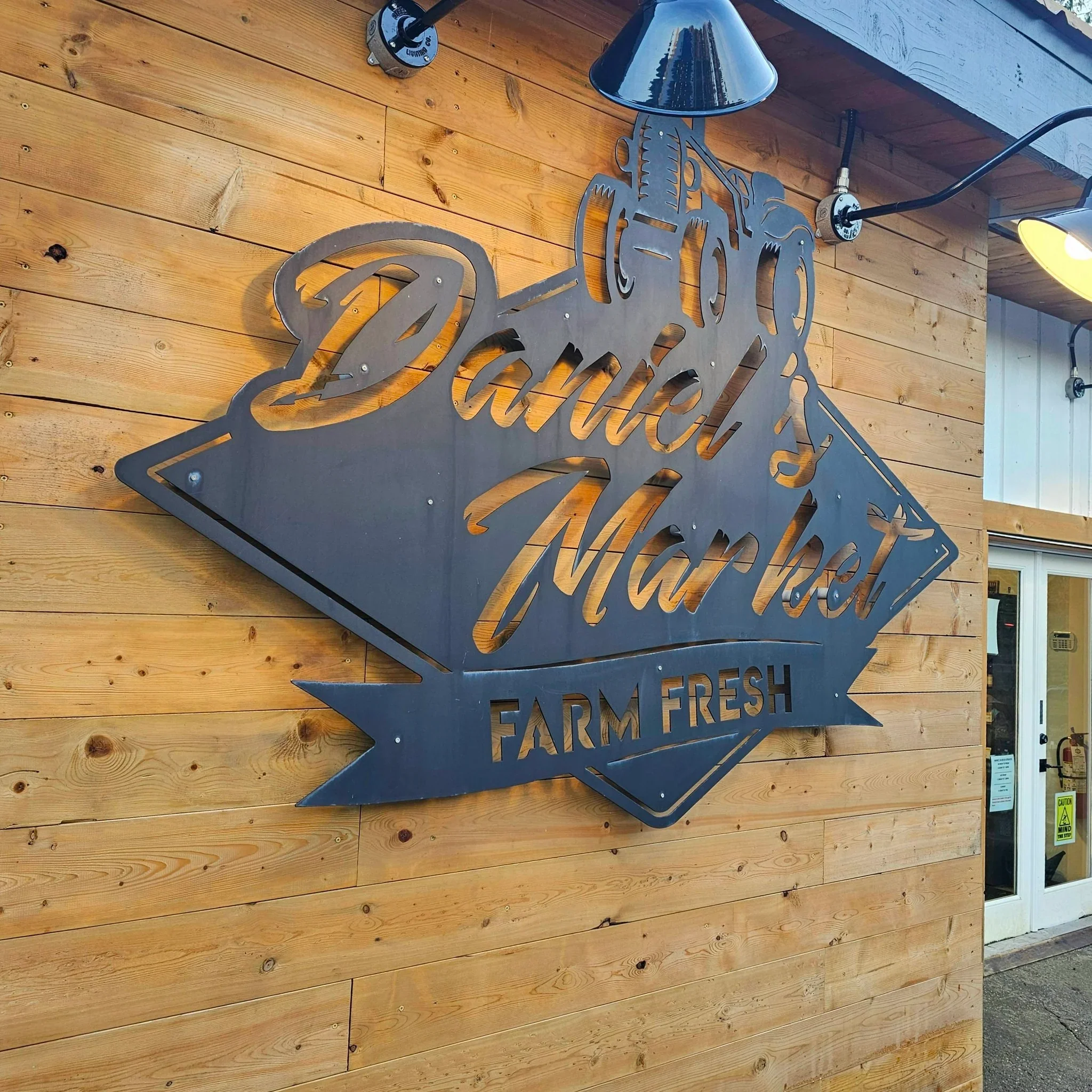 Logo for Daniel's Market featuring a black tractor illustration above the store name, with the words "Farm Fresh" in white on a green banner.