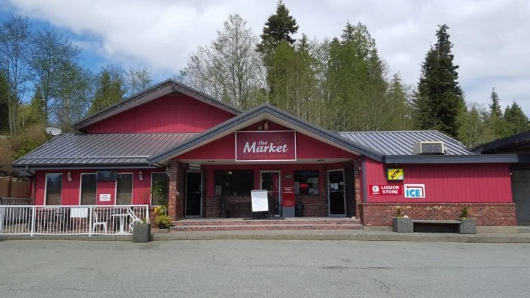 Red building with a sign that says "the Market" and storefront windows, surrounded by trees.