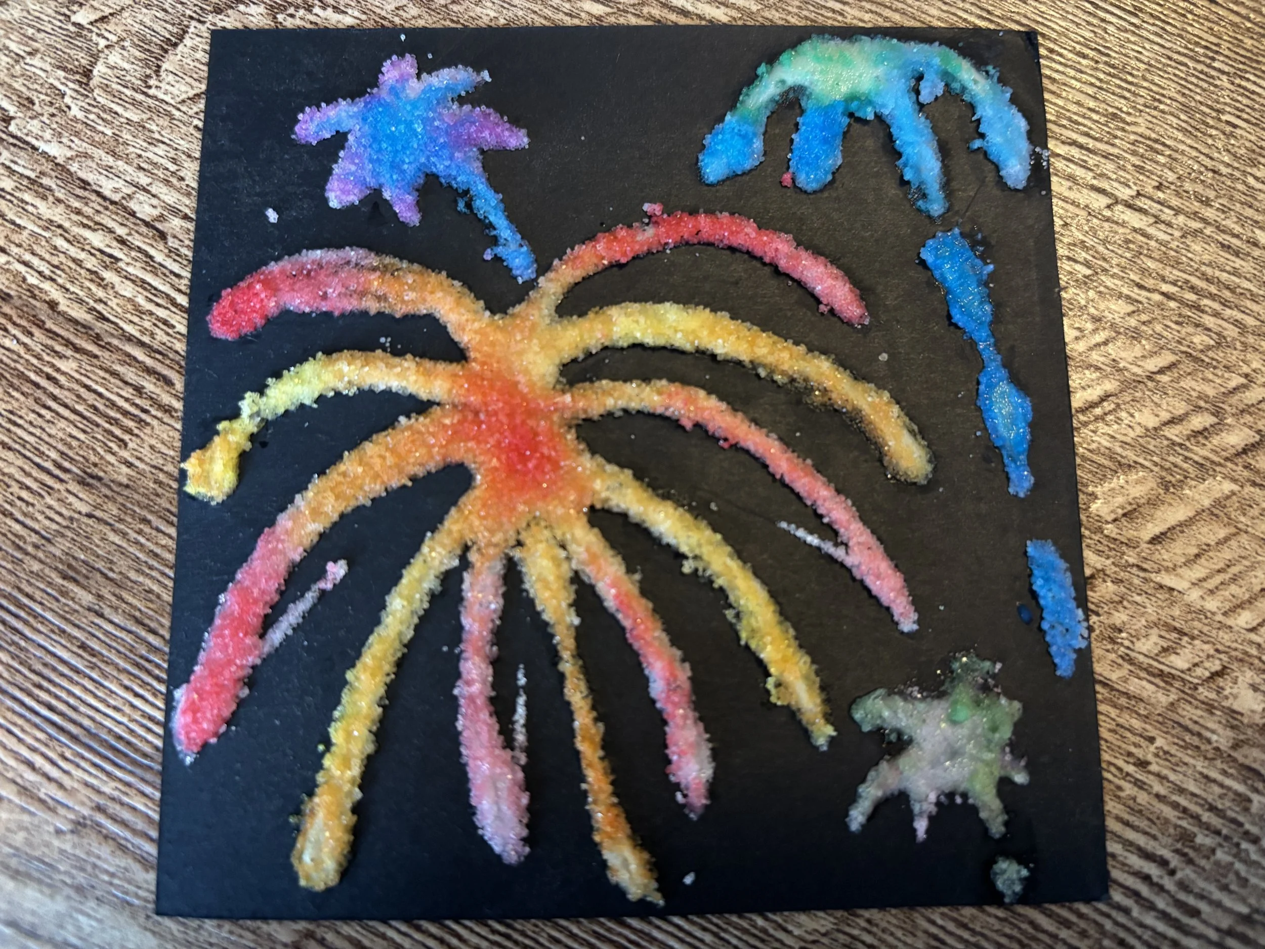 A child's art project where you glue salt to a black piece of paper, then paint the salt with water colors.